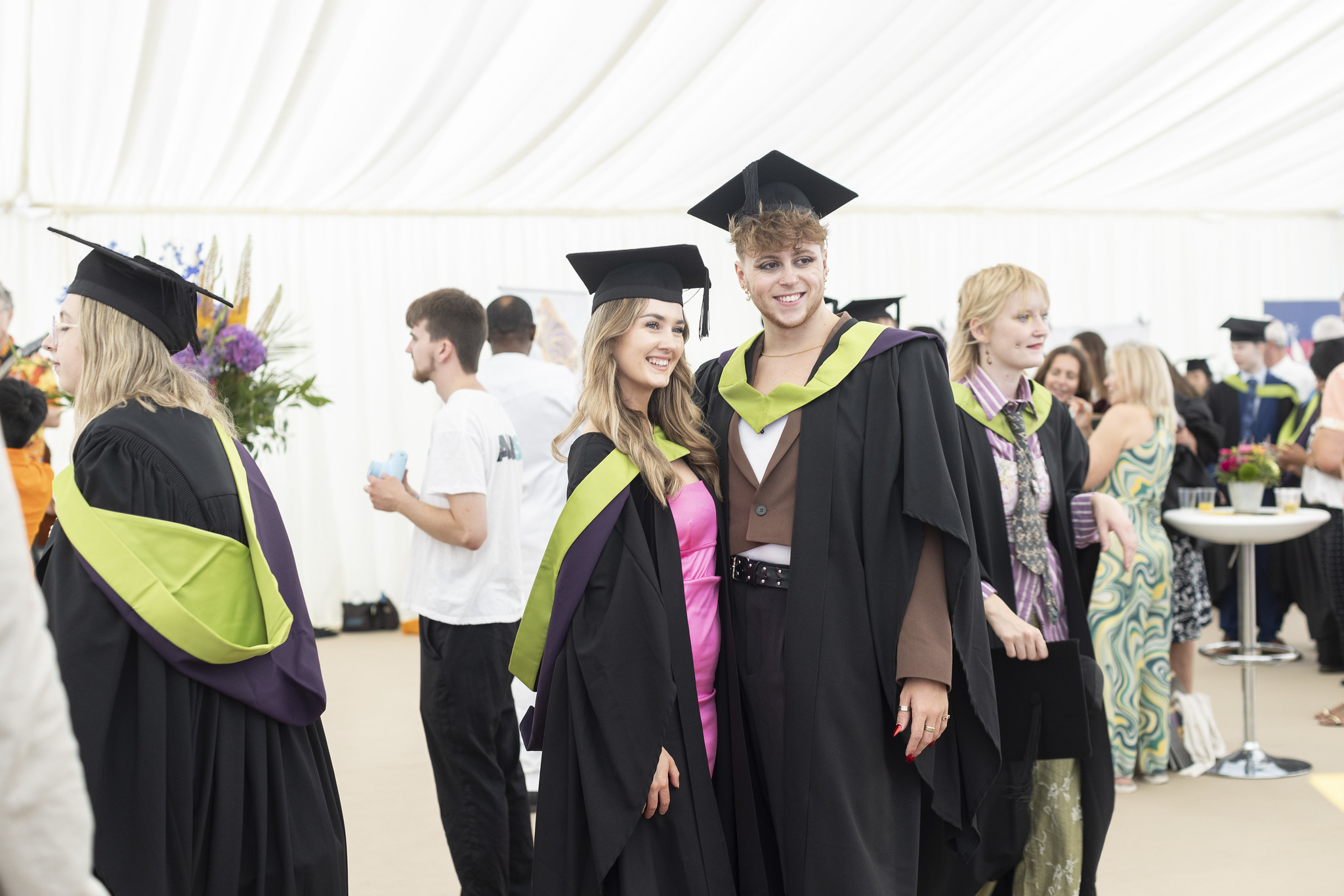 Two students in graduate gowns posing for the camera in a white marquee.