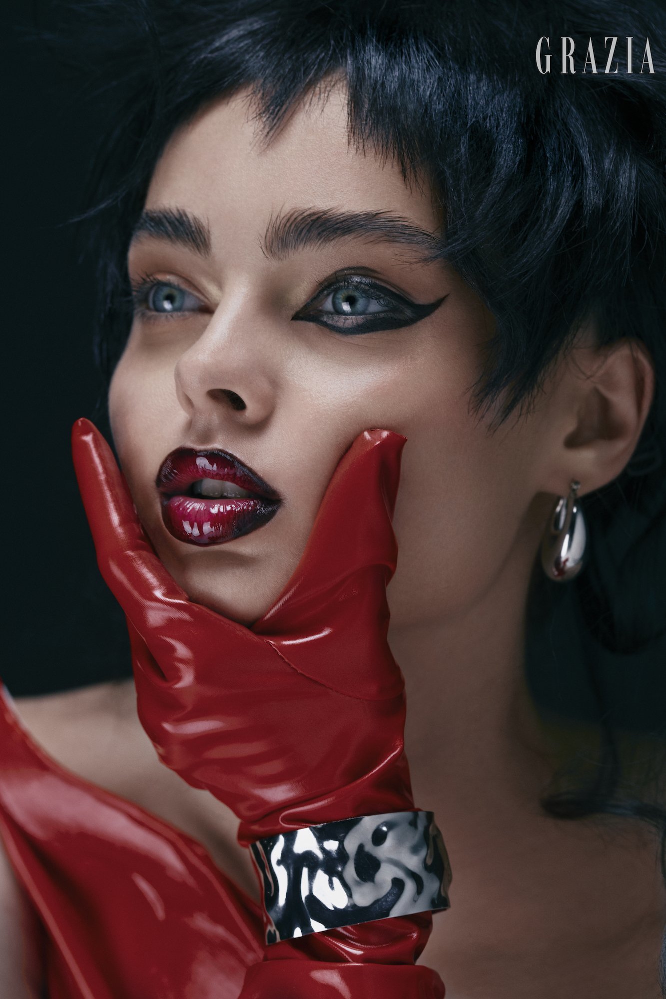 A woman face, wearing makeup and being held up by a red leather glove.