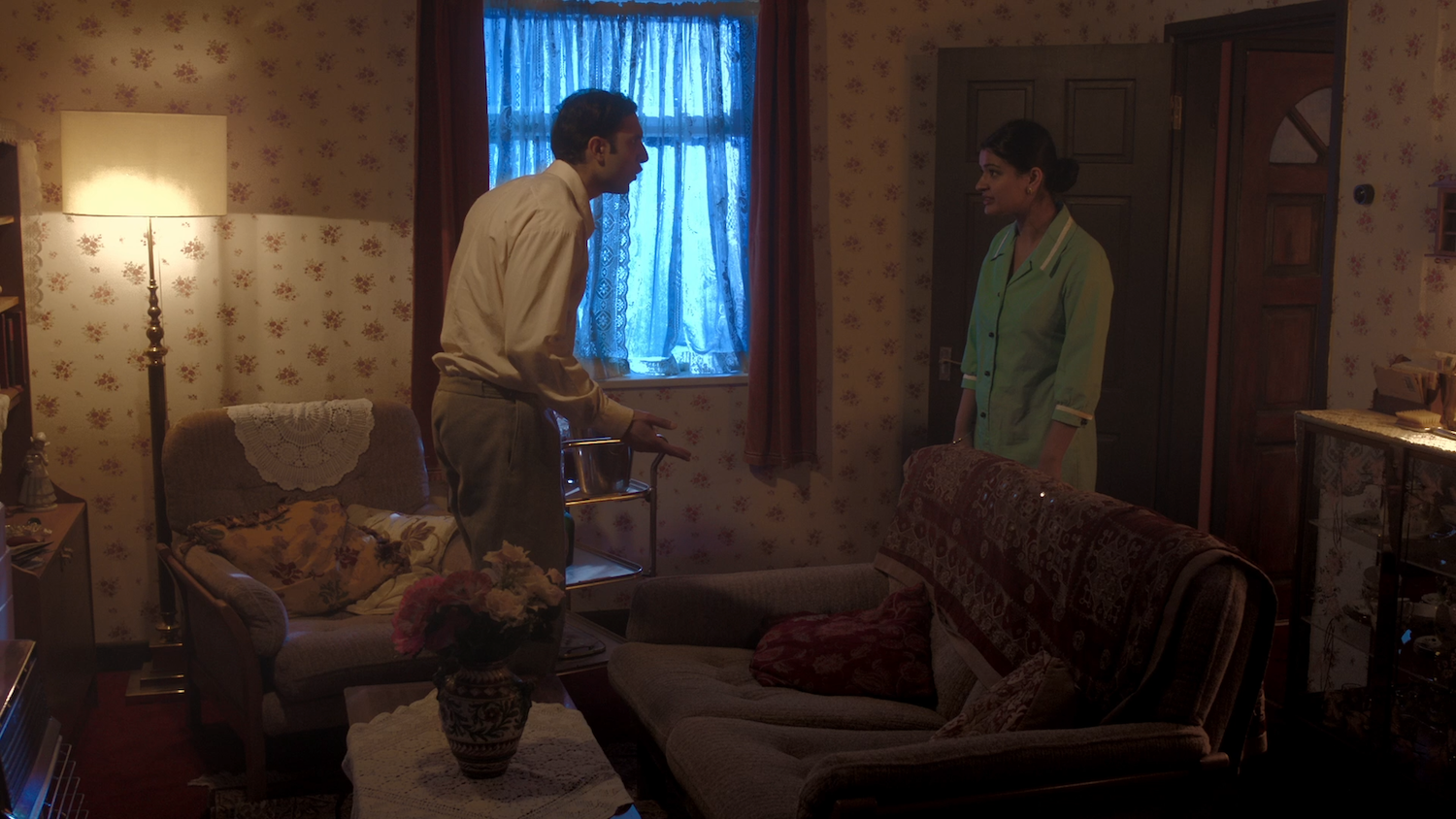 Film still of a couple arguing in a 70s-style living room, dim lighting.