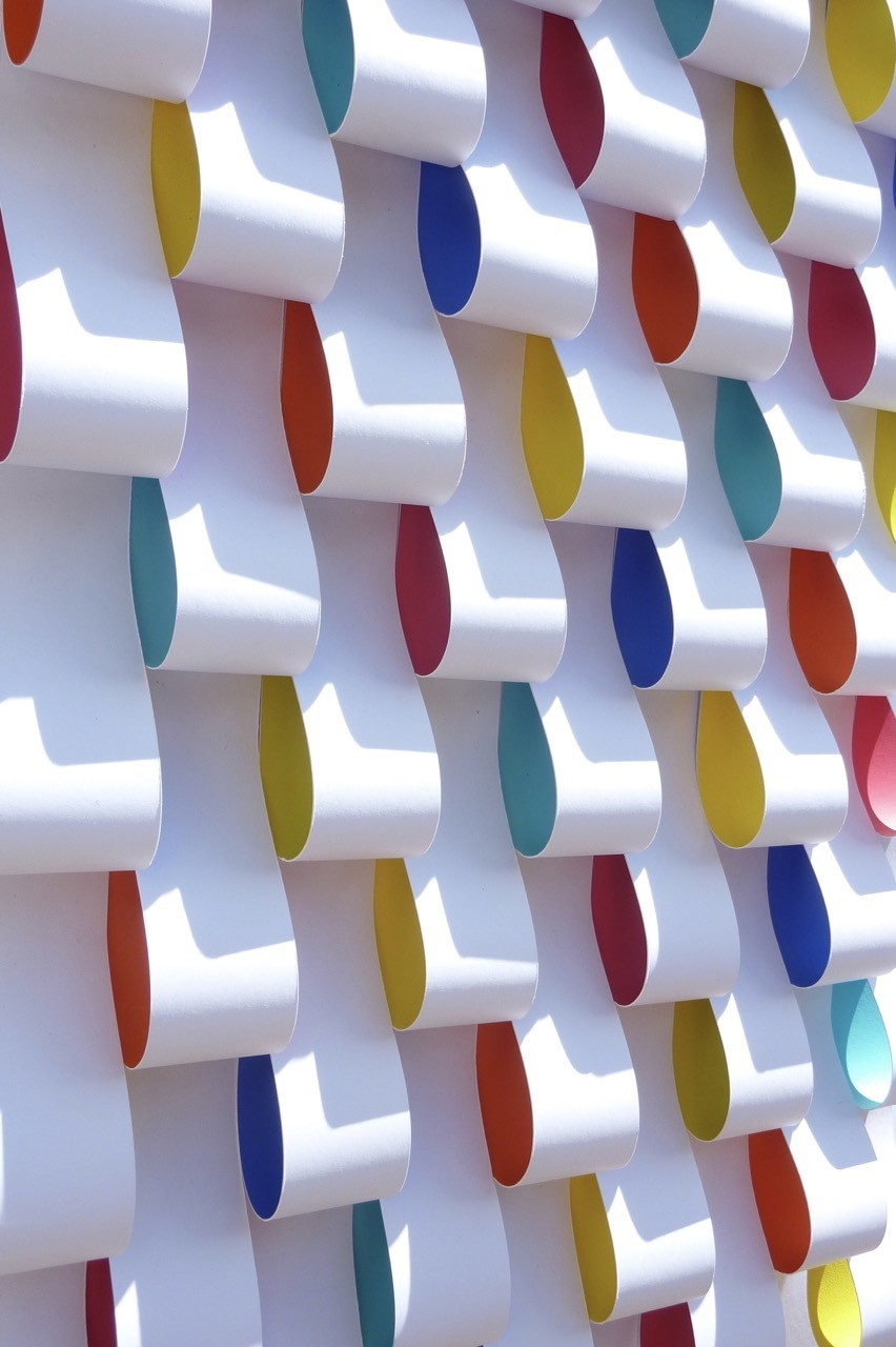 White cylindrical tubes arranged in rows with coloured oval ends in red, blue, yellow, green, and orange creating a geometric pattern.