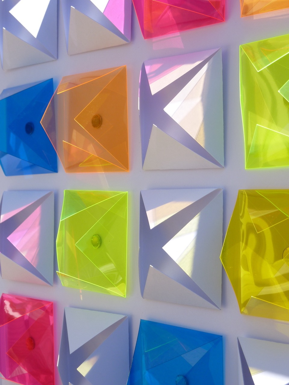 Geometric pattern with alternating translucent coloured squares and white angular recessed shapes arranged in grid formation.
