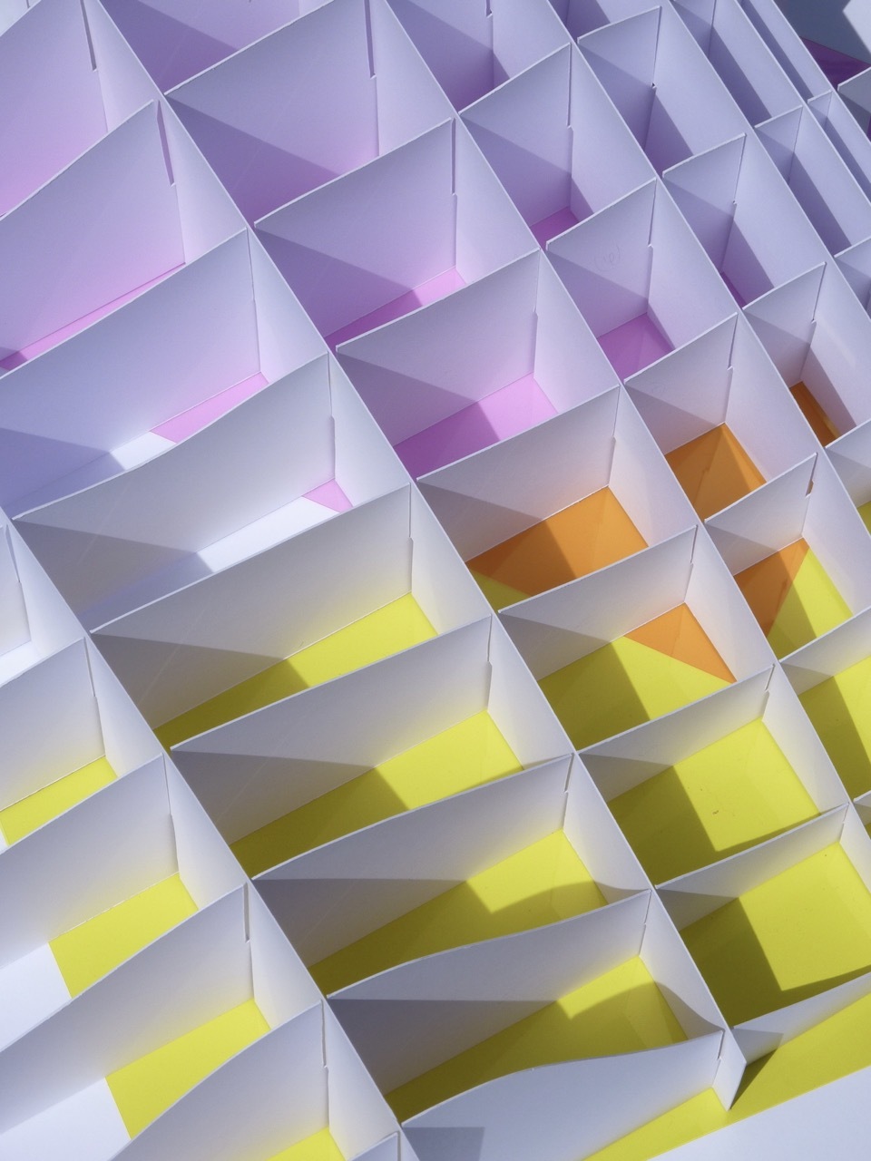 Geometric pattern of white triangular shapes creating diamond-like grid. Purple tones at top transitioning to orange and bright yellow at bottom.