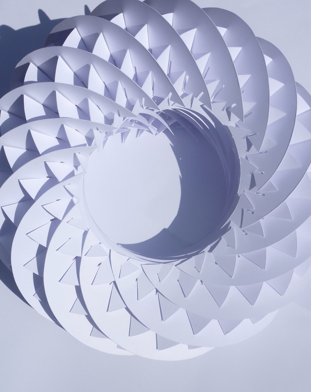 Spiral composition with metallic silver circular forms featuring triangular geometric patterns, creating depth through overlapping layers against pale grey background.