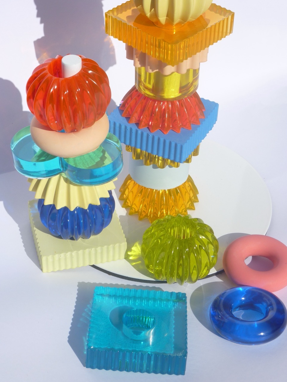 Colourful translucent plastic objects with ridged surfaces stacked and arranged on white surface. Orange, blue, green, yellow shapes.
