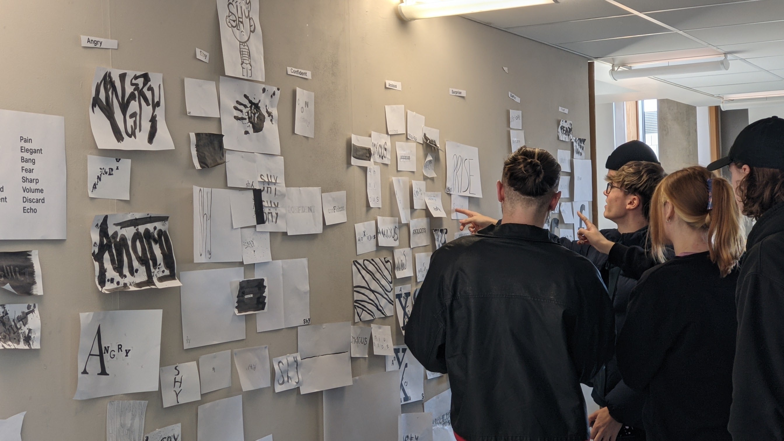 students working in groups and pointing at ideas written on paper and pinned to a wall