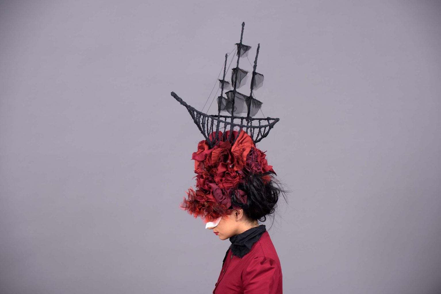 A model viewed side-on wearing a headdress with a ship in it.