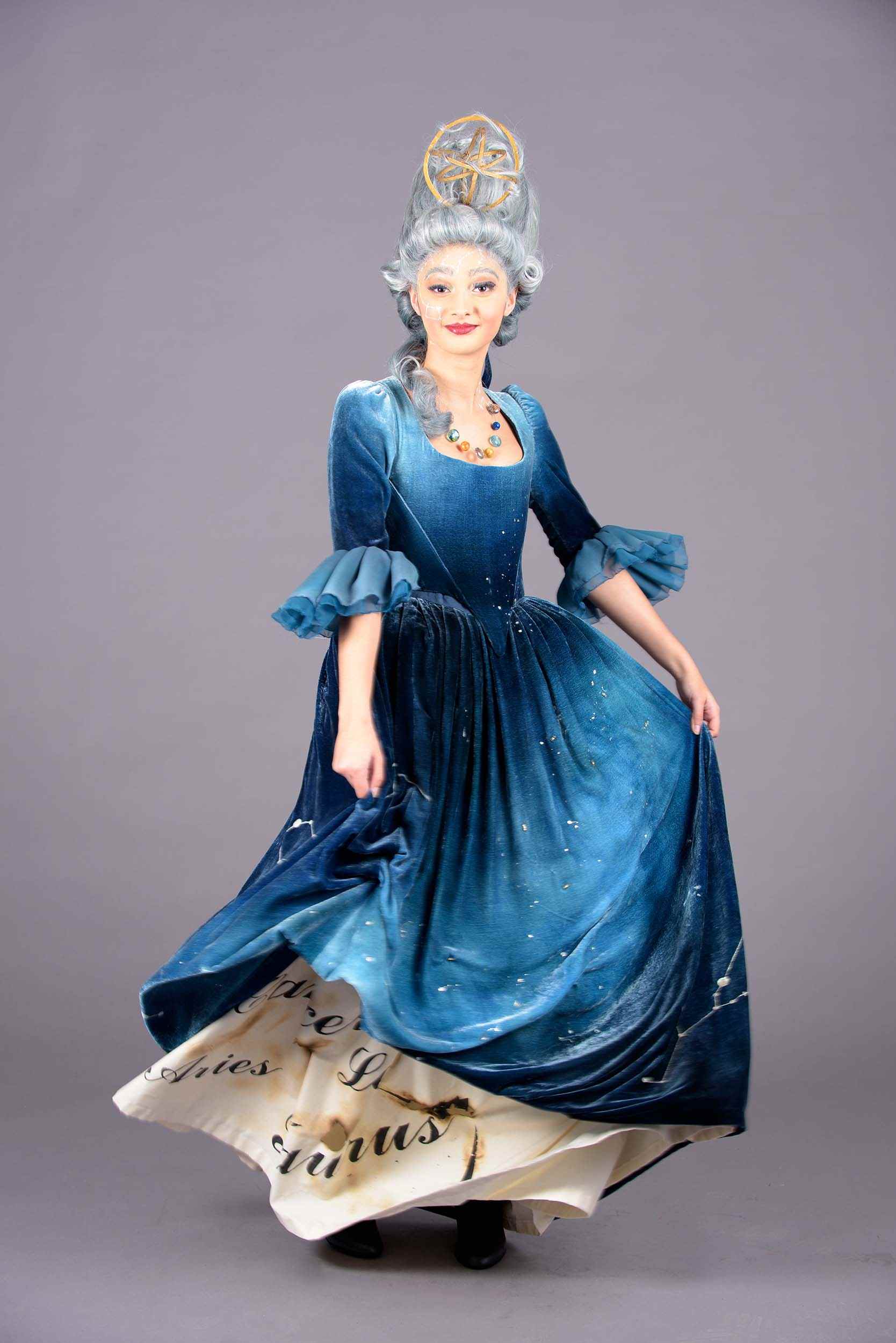 A person standing against a plain background in an 18th century-style costume and wig.