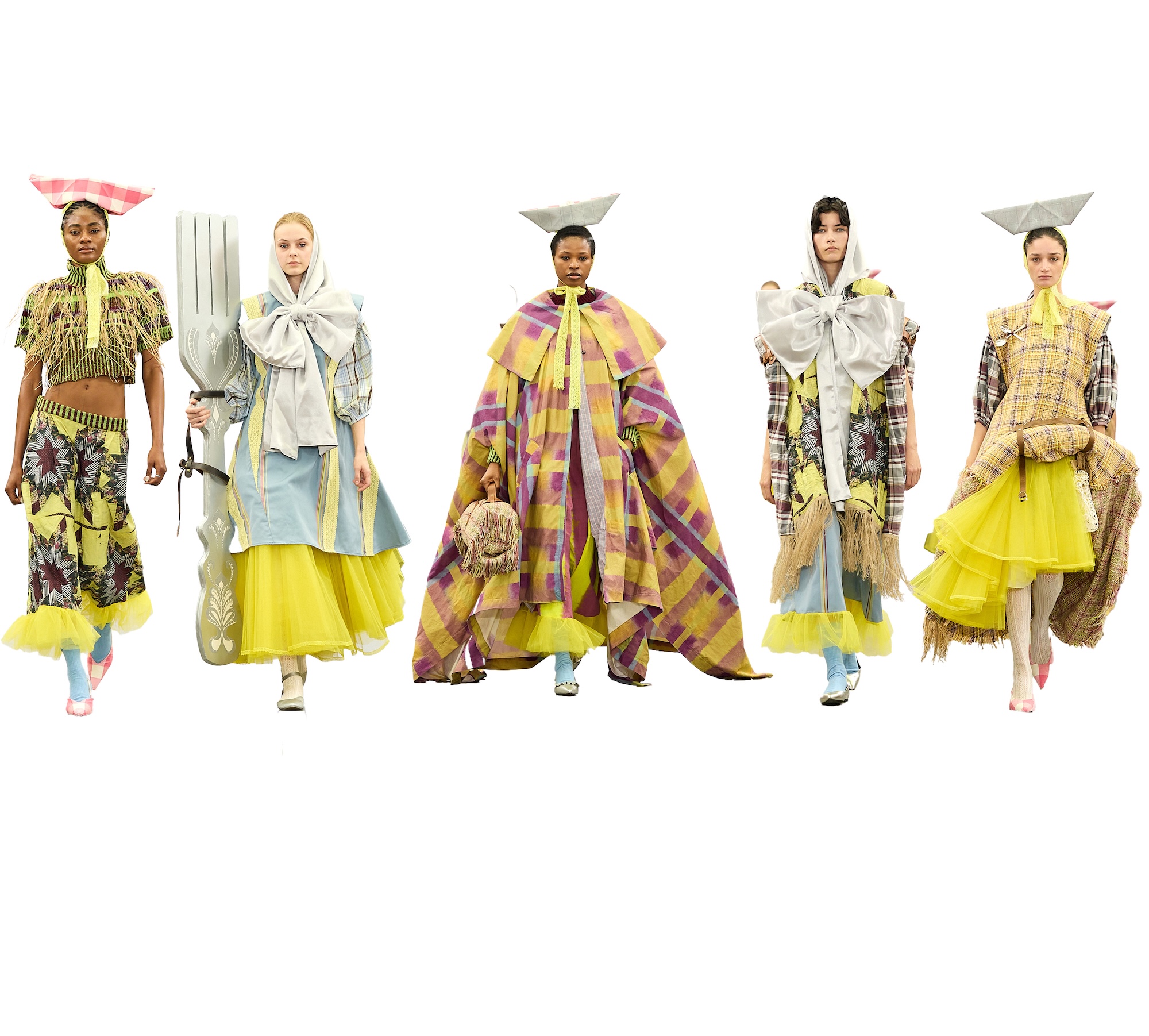 Five fashion models in avant-garde outfits walk on a white runway, wearing oversized layered garments in yellow, grey and plaid.