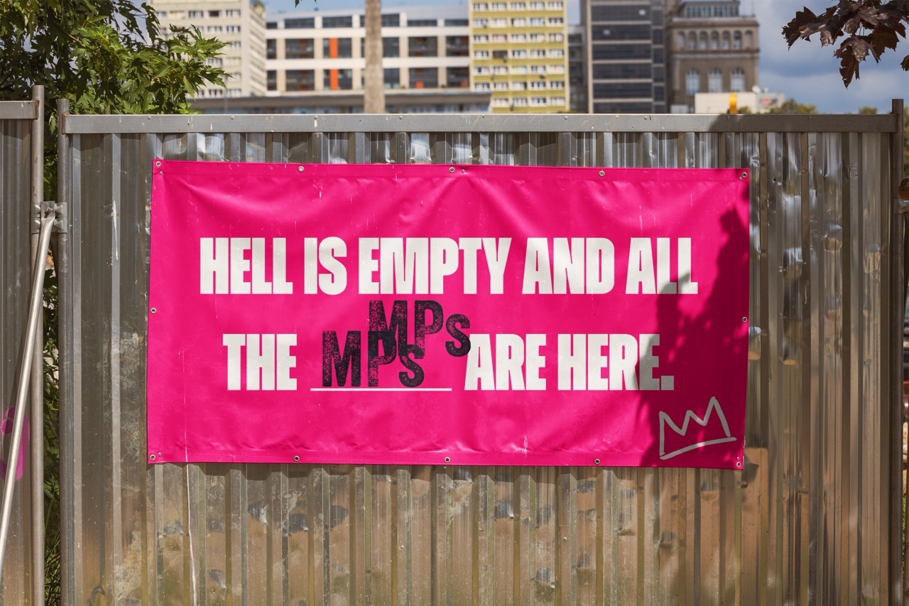 Mock-up of a pink banner on a metal wall with distorted white/purple text: 'HELL IS EMPTY AND THE MPs ARE HERE'.