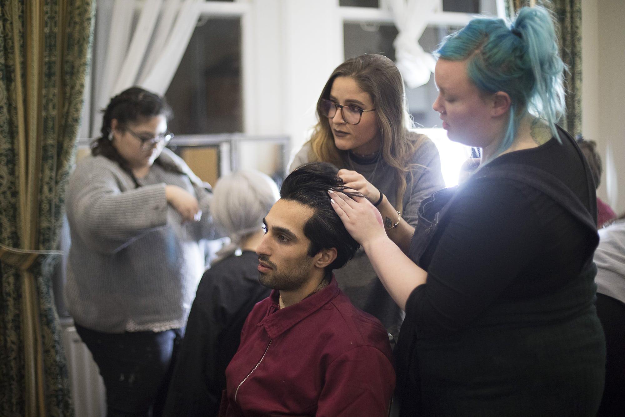 Two people work on the hair of a model who is seated.