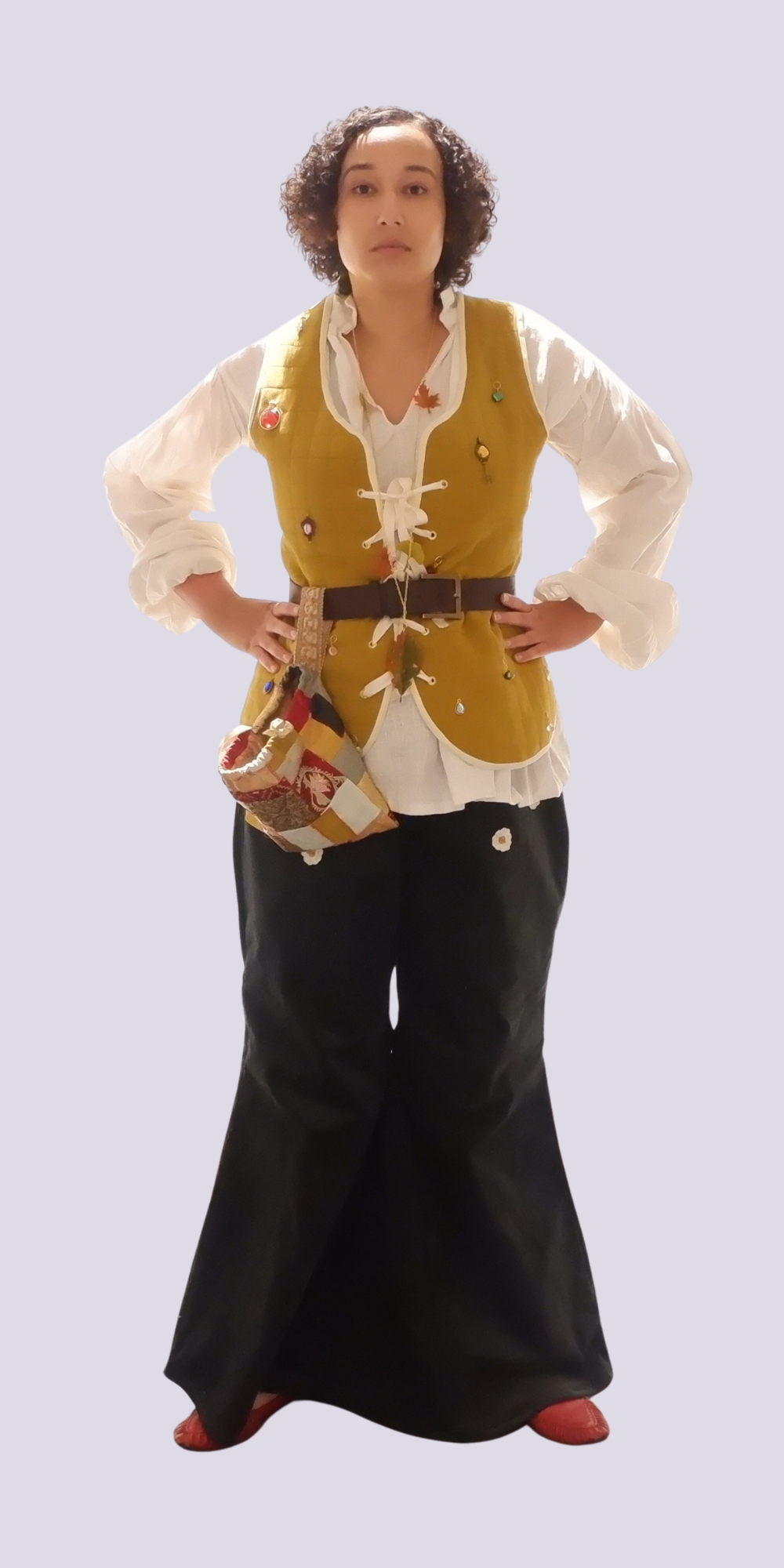 Woman in period costume with white blouse, yellow waistcoat, brown belt, black skirt, hands on hips against white background.