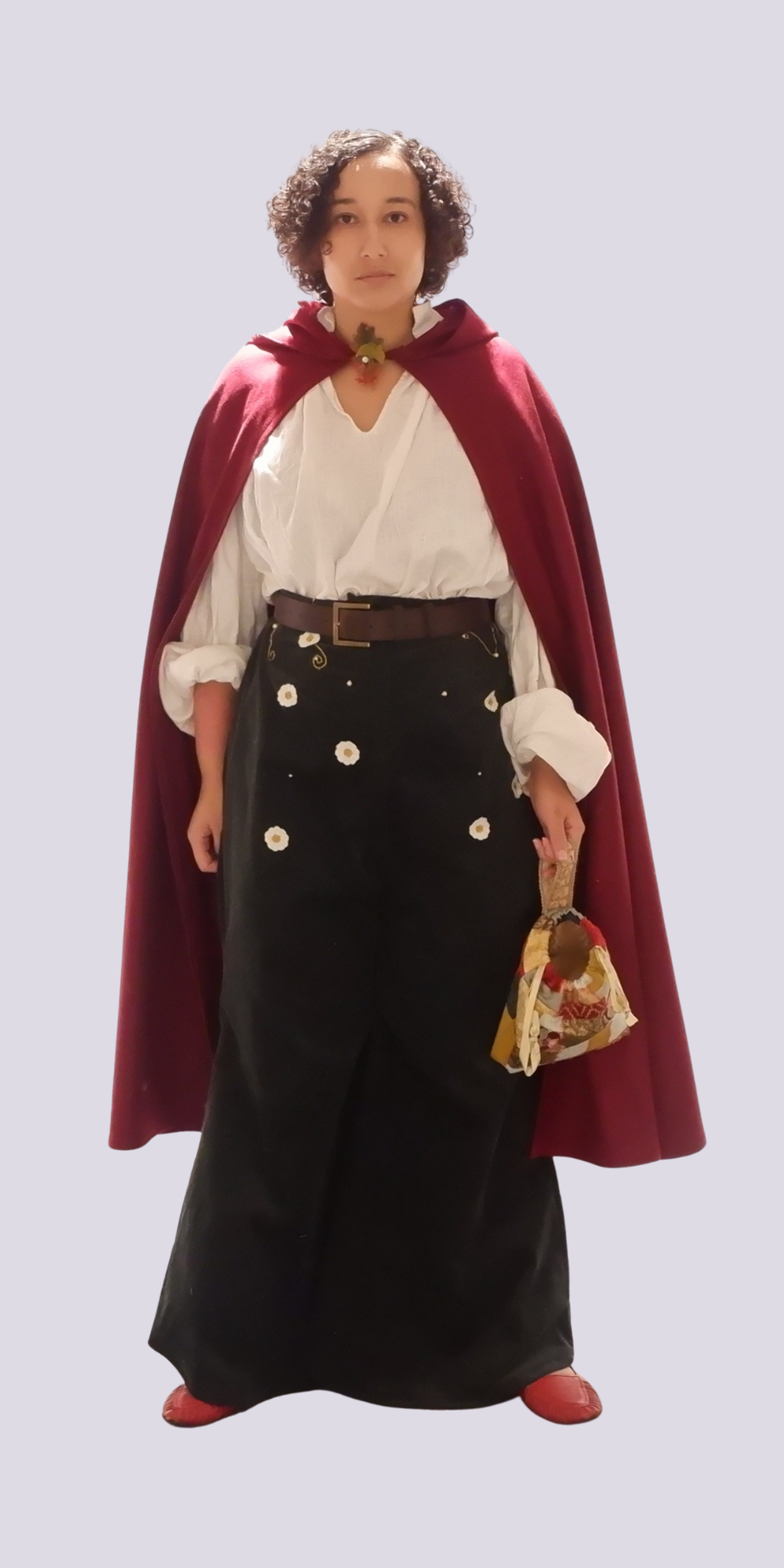 Person in historical costume with burgundy hooded cloak, white blouse, dark green skirt with buttons, and small handbag on white background.