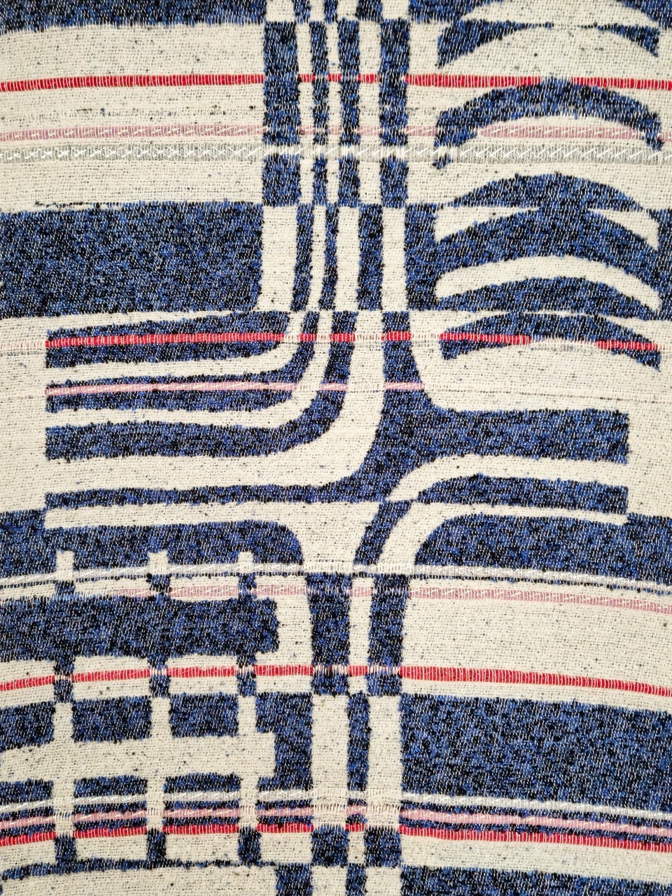 Woven textile with abstract geometric pattern in navy blue, cream, and red threads forming curved and linear shapes.