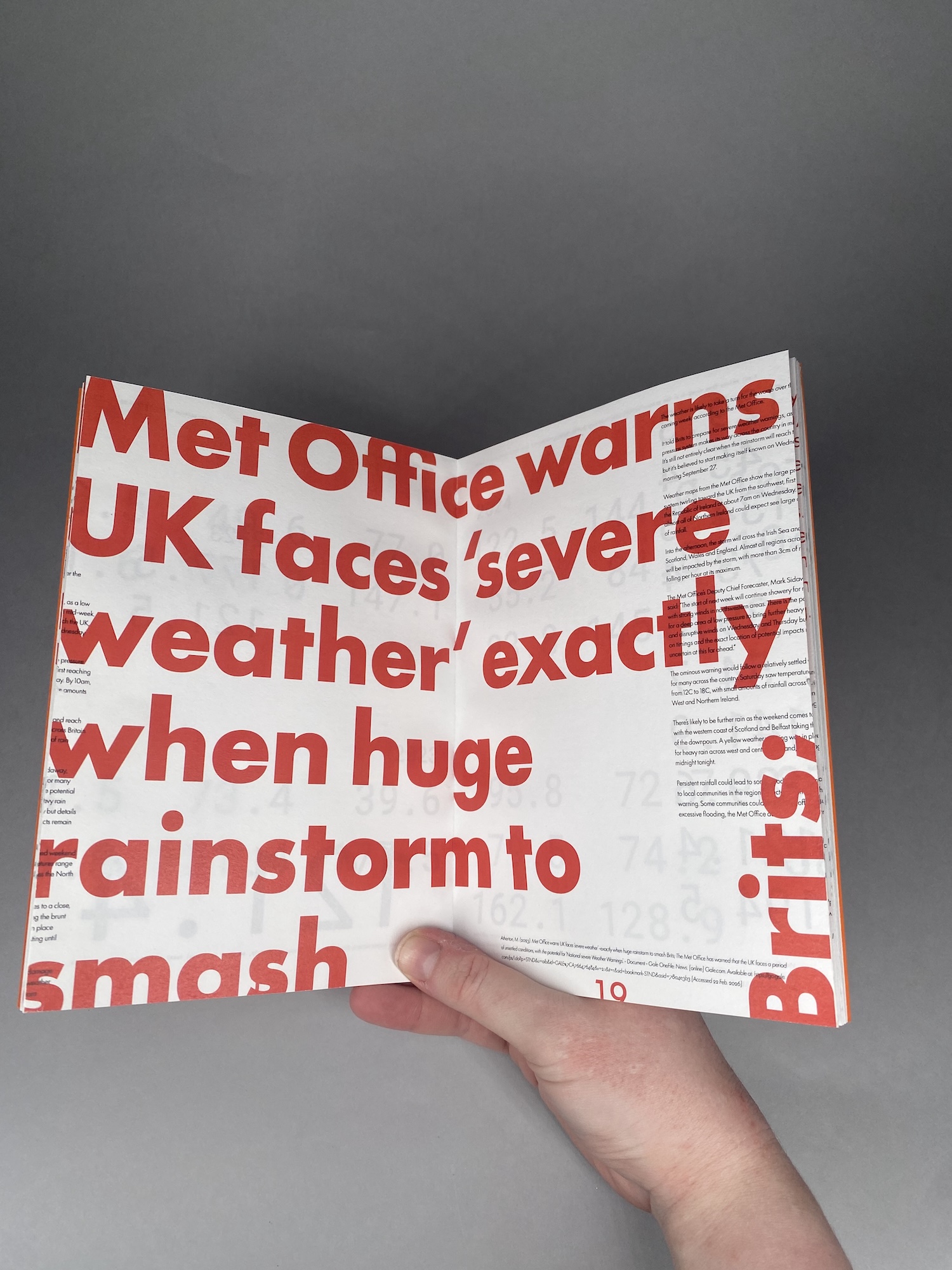 A hand holds an open newspaper showing a red headline about the Met Office warning of severe weather and a huge rainstorm, against a grey background.