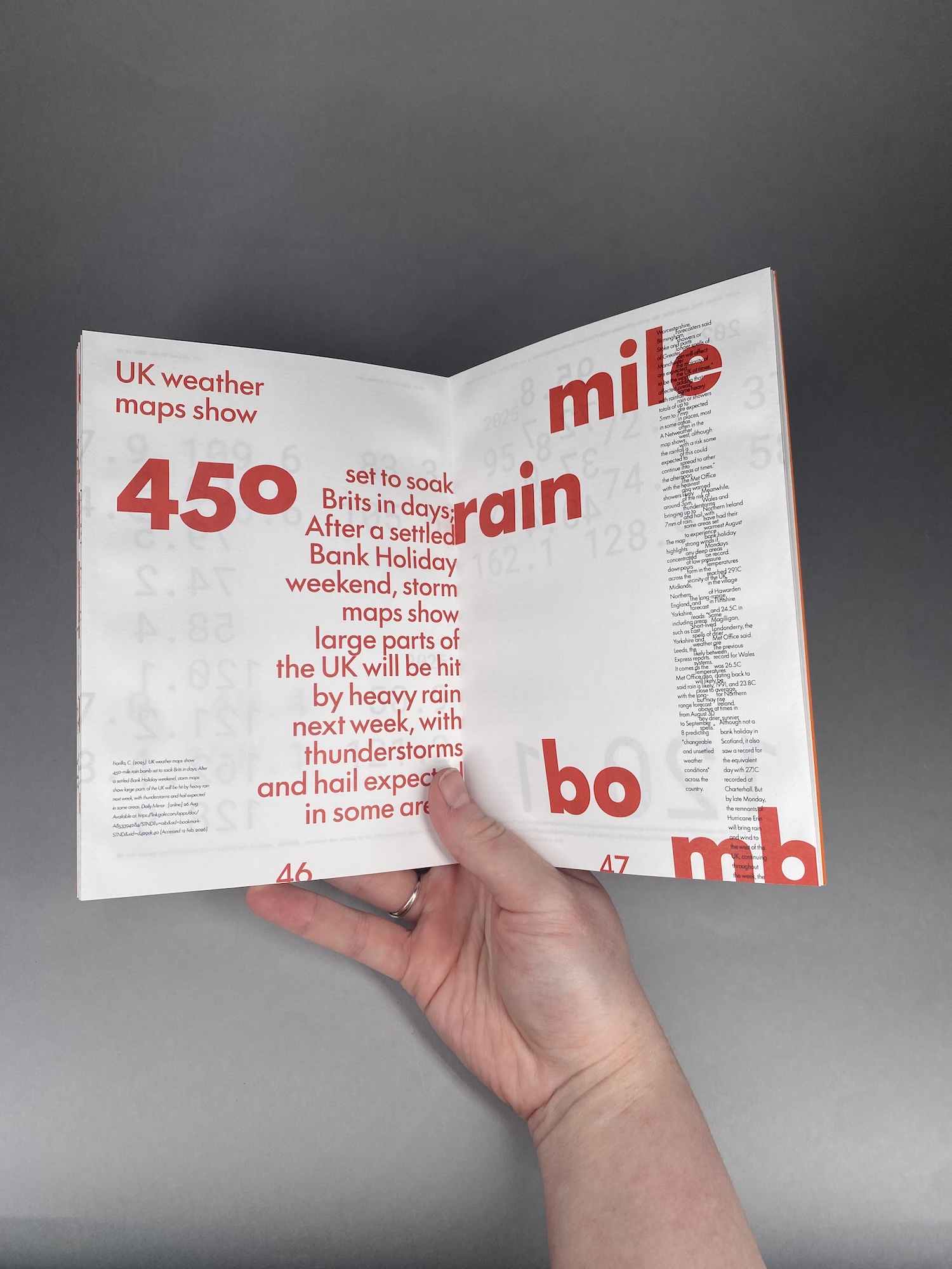 A hand holds open a folded magazine spread with large red weather-related typography and columns of small text on a grey background.