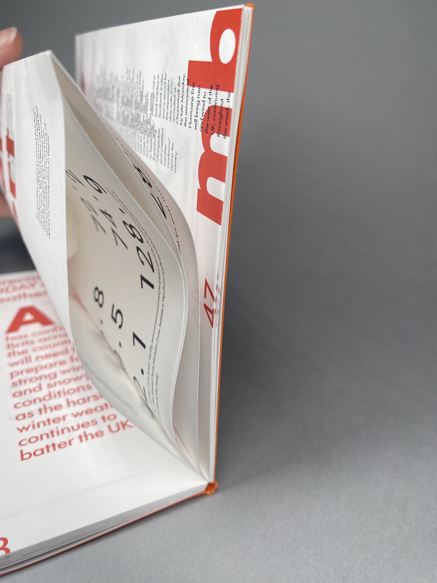 An open magazine with a curled page and a circular cut-out insert, resting on a grey surface.