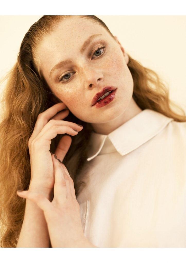 Portrait of a lady wearing red lipstick, tilting their head and touching their face.