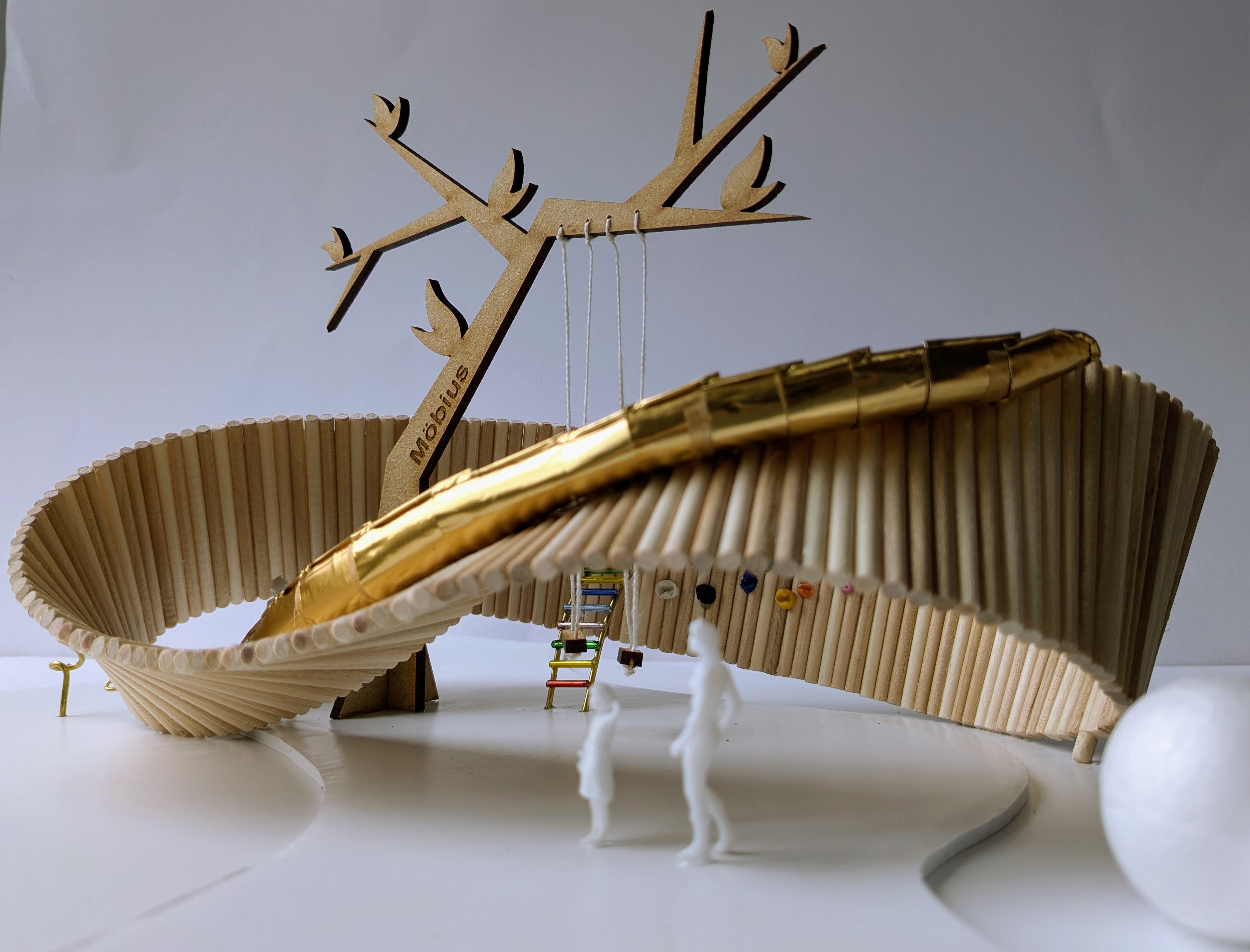 Curved small-scale wooden pavilion structure with vertical slats, featuring branched tree-like element extending upwards. White figures and ladder nearby.