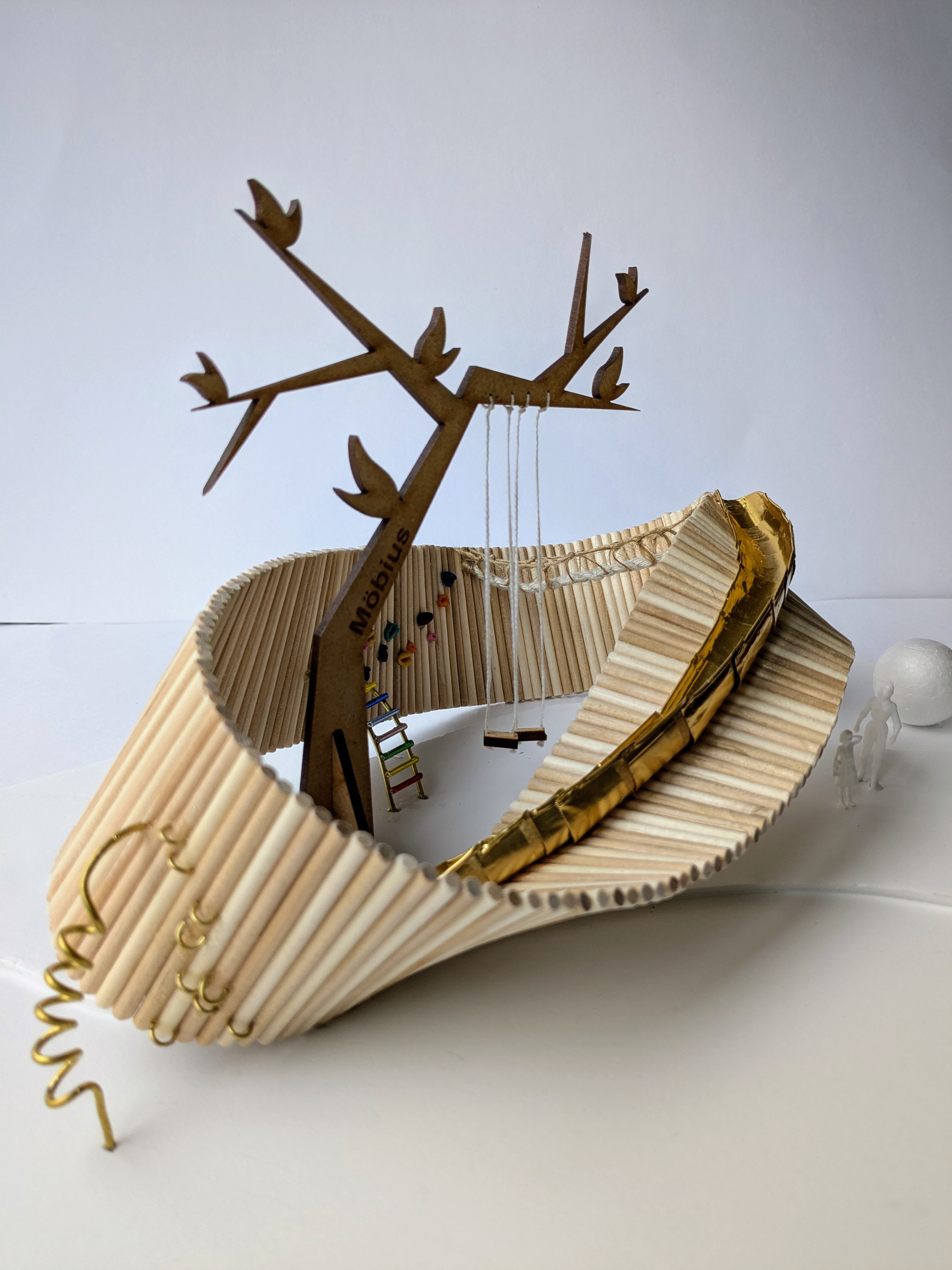Wooden model of a flowing sculpture and tree in the middle on white surface against grey background.