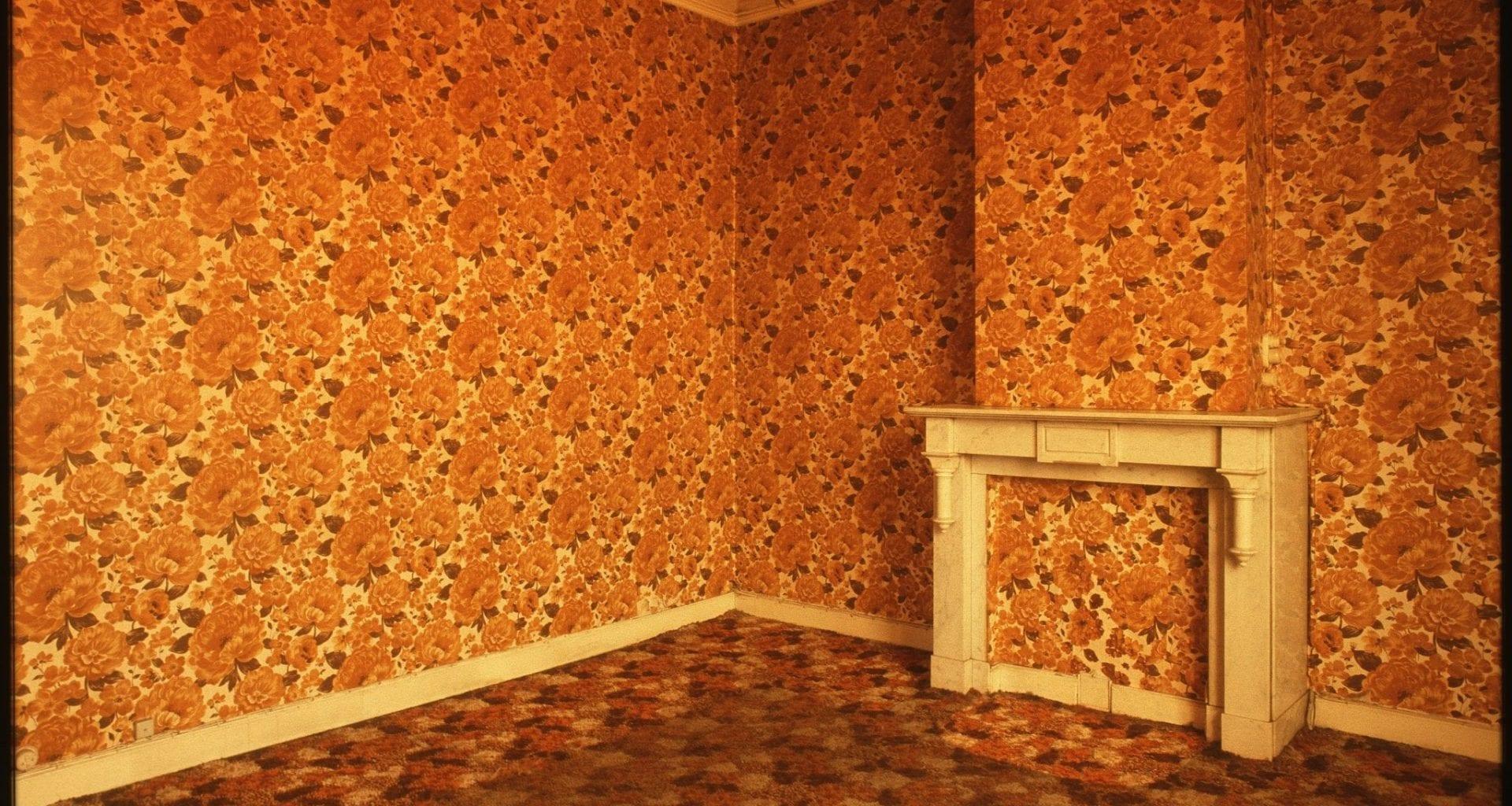 A room covered completely (top to bottom, including a fire place) in floral orange wallpaper