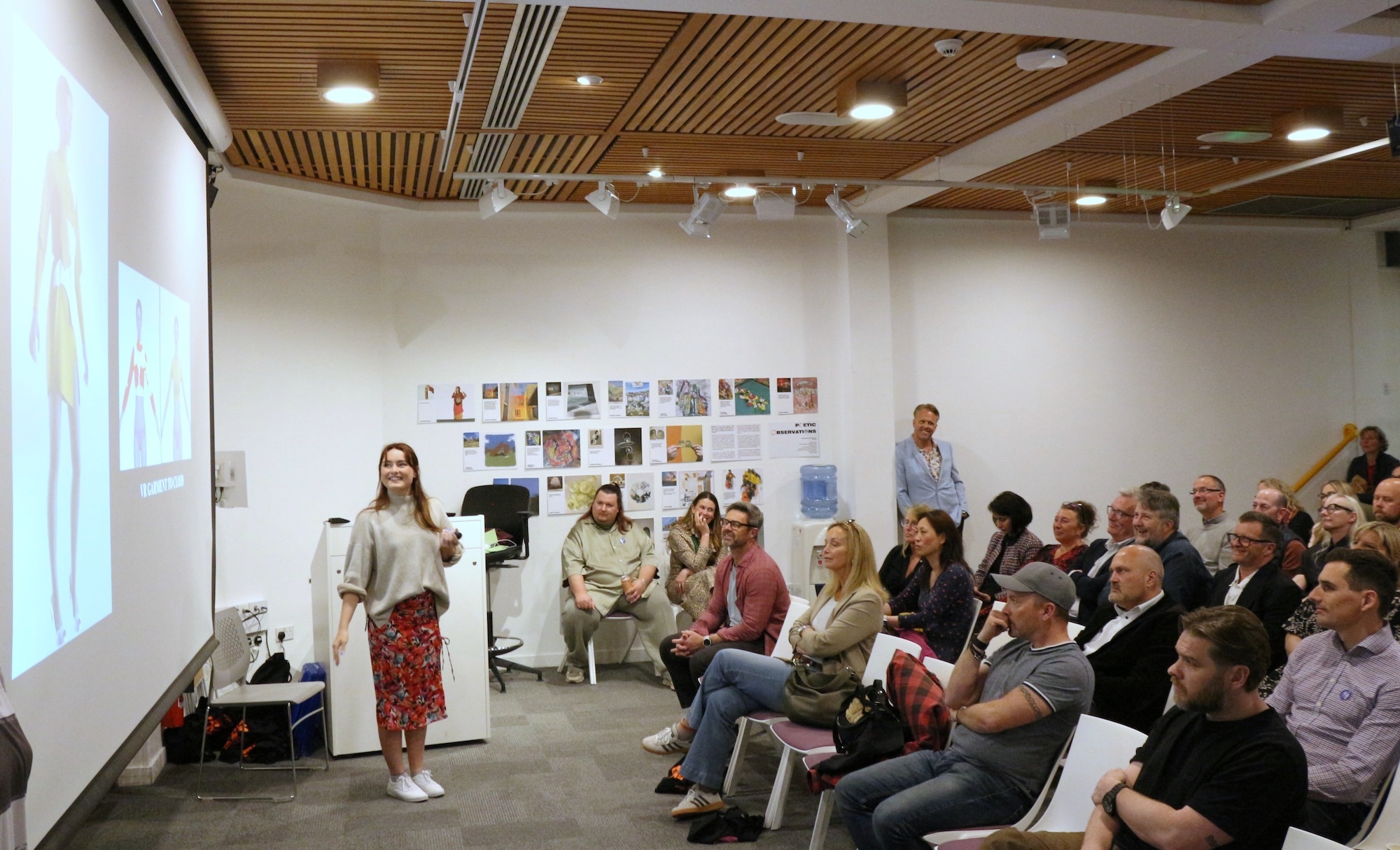 MA Digital Fashion Innovation student H New stands in front of a large screen giving a presentation in front of a large group of people at Arts University Bournemouth.