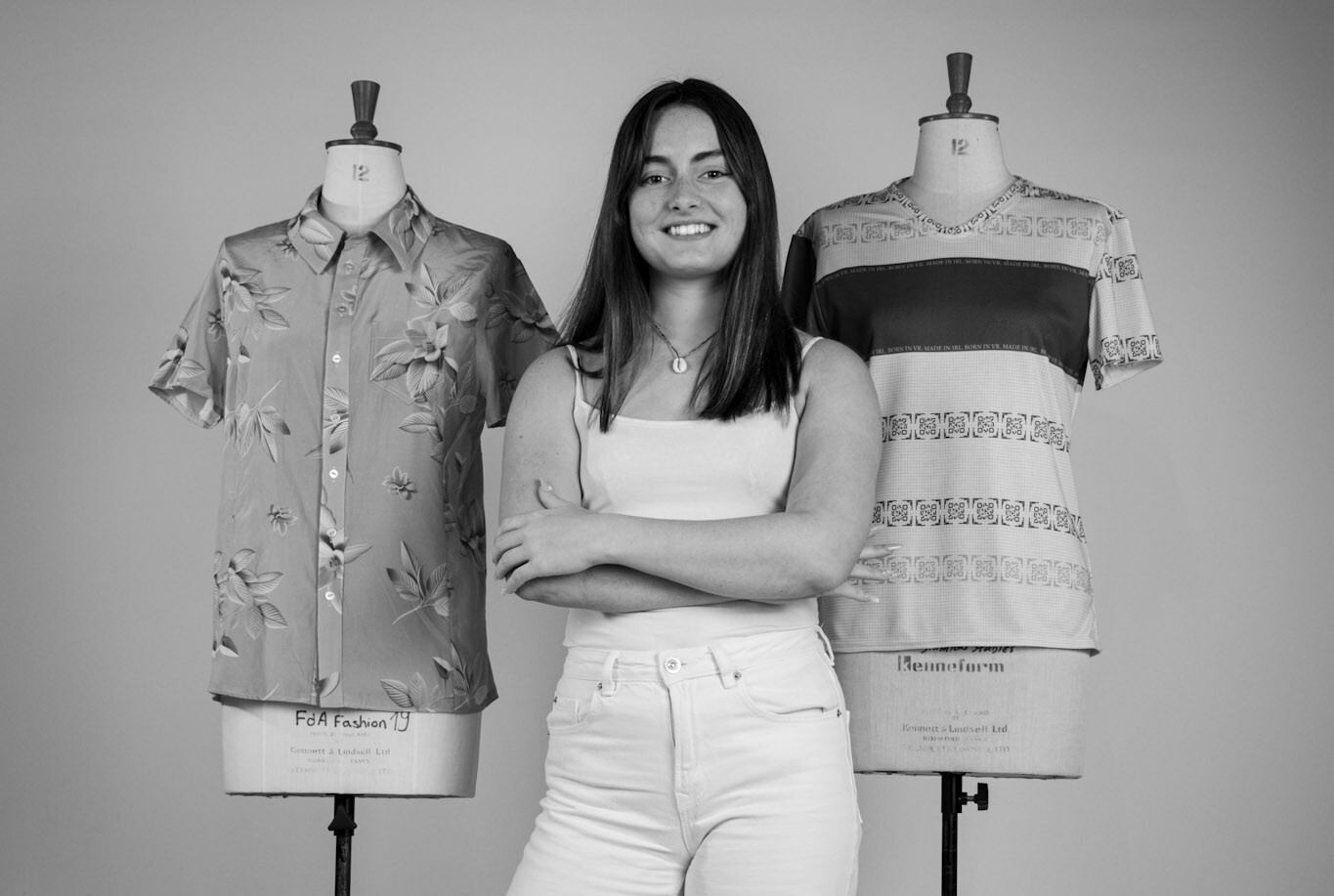 H New standing between two clothing mannequins displaying patterned shirts in black and white image.