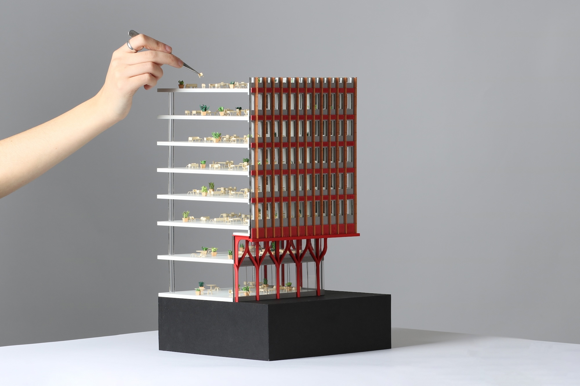 A BA (Hons) Modelmaking student applies a detail to an architectural model on a black stand with a pair of tweezers.