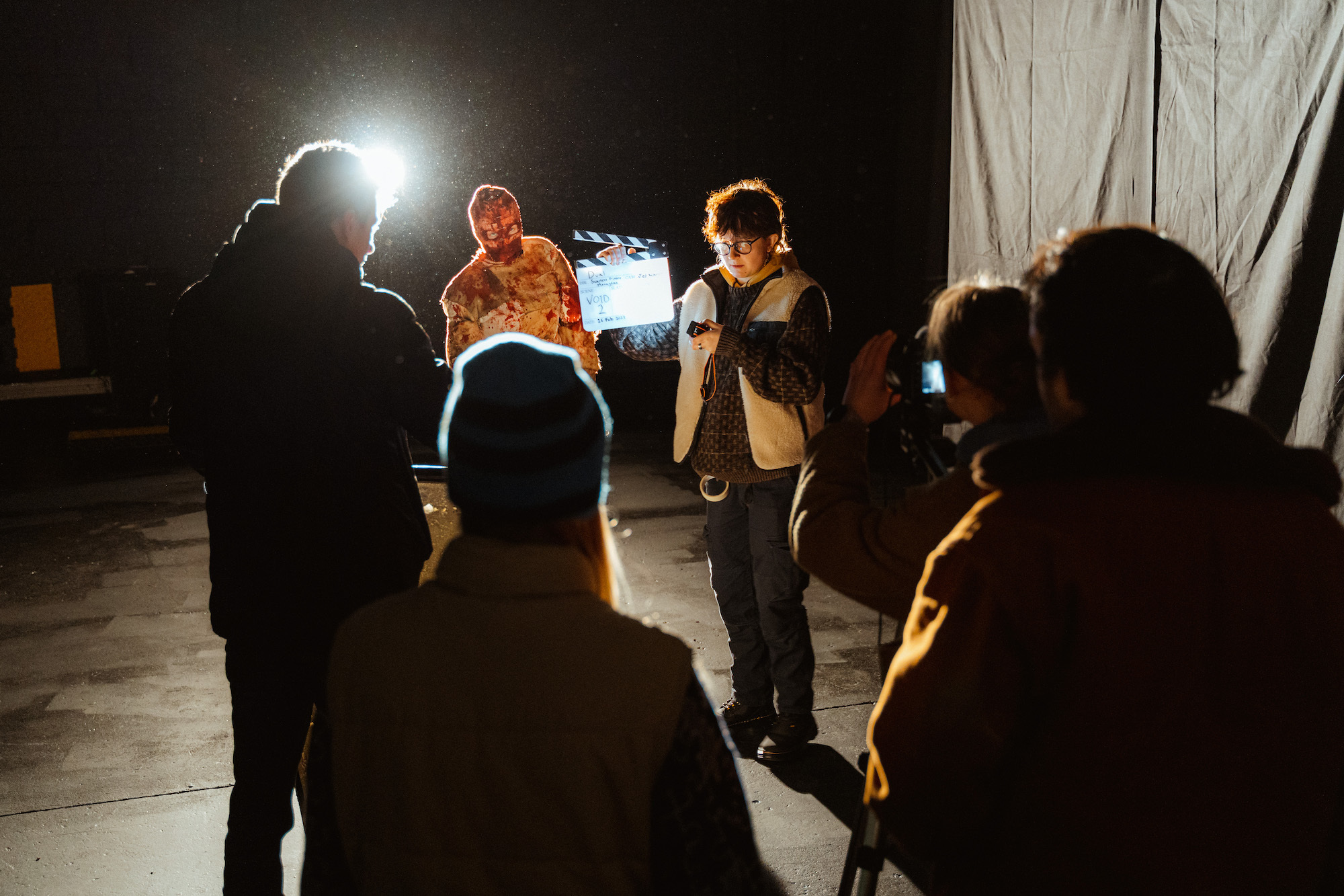 Film crew in dramatic lighting with a person in prosthetic body bandages, blood.