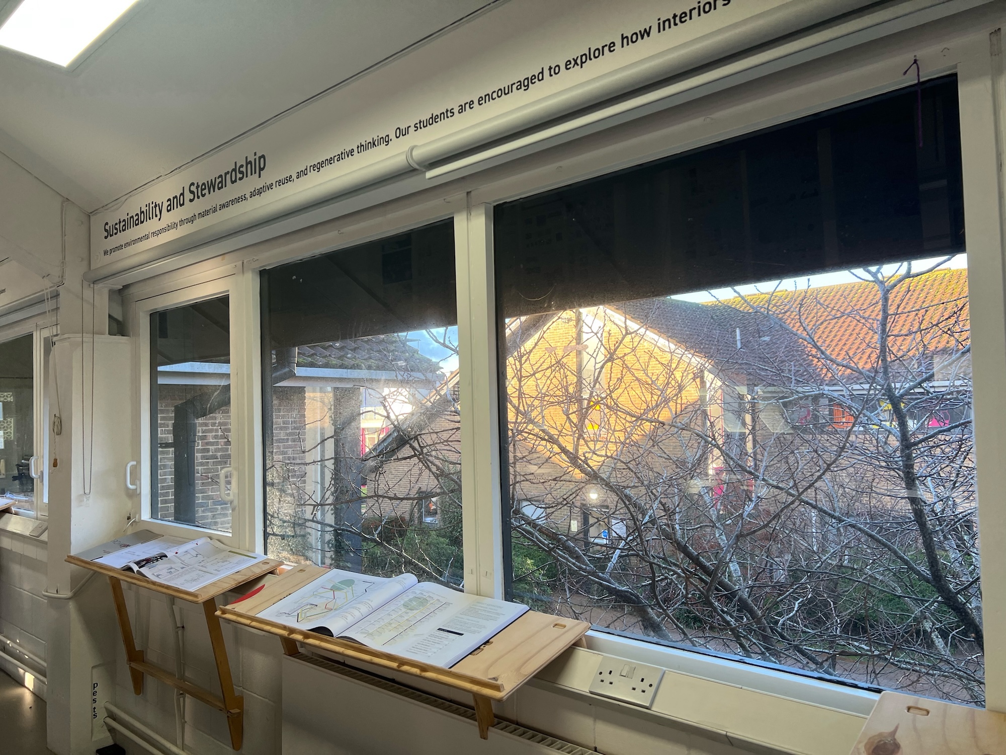 Large windows with white frames showing autumn trees and buildings outside. Wooden lecterns with papers positioned along windowsill.