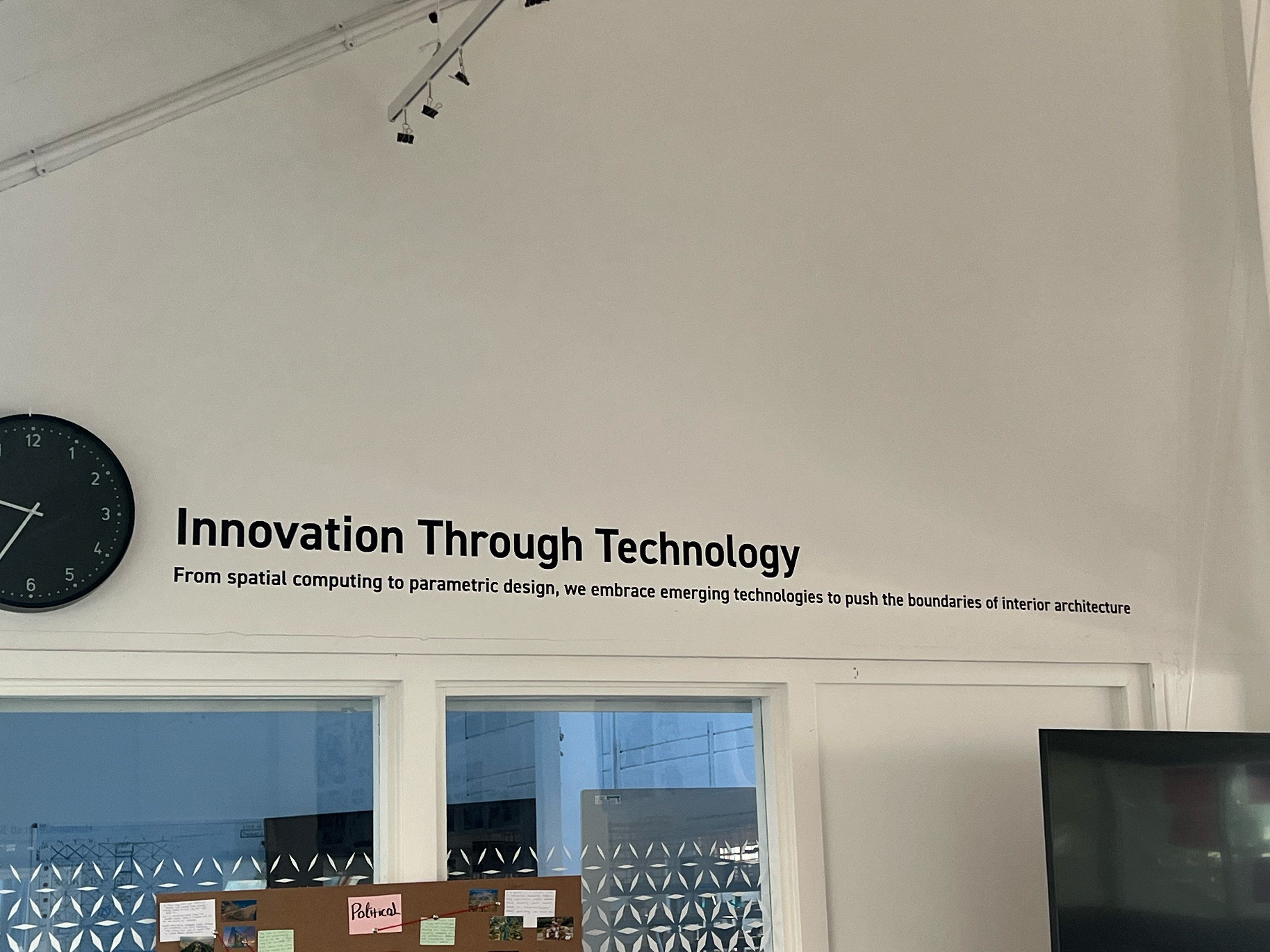 White wall with "Innovation Through Technology" text in black, track lighting above, blue windows and geometric patterned display below.