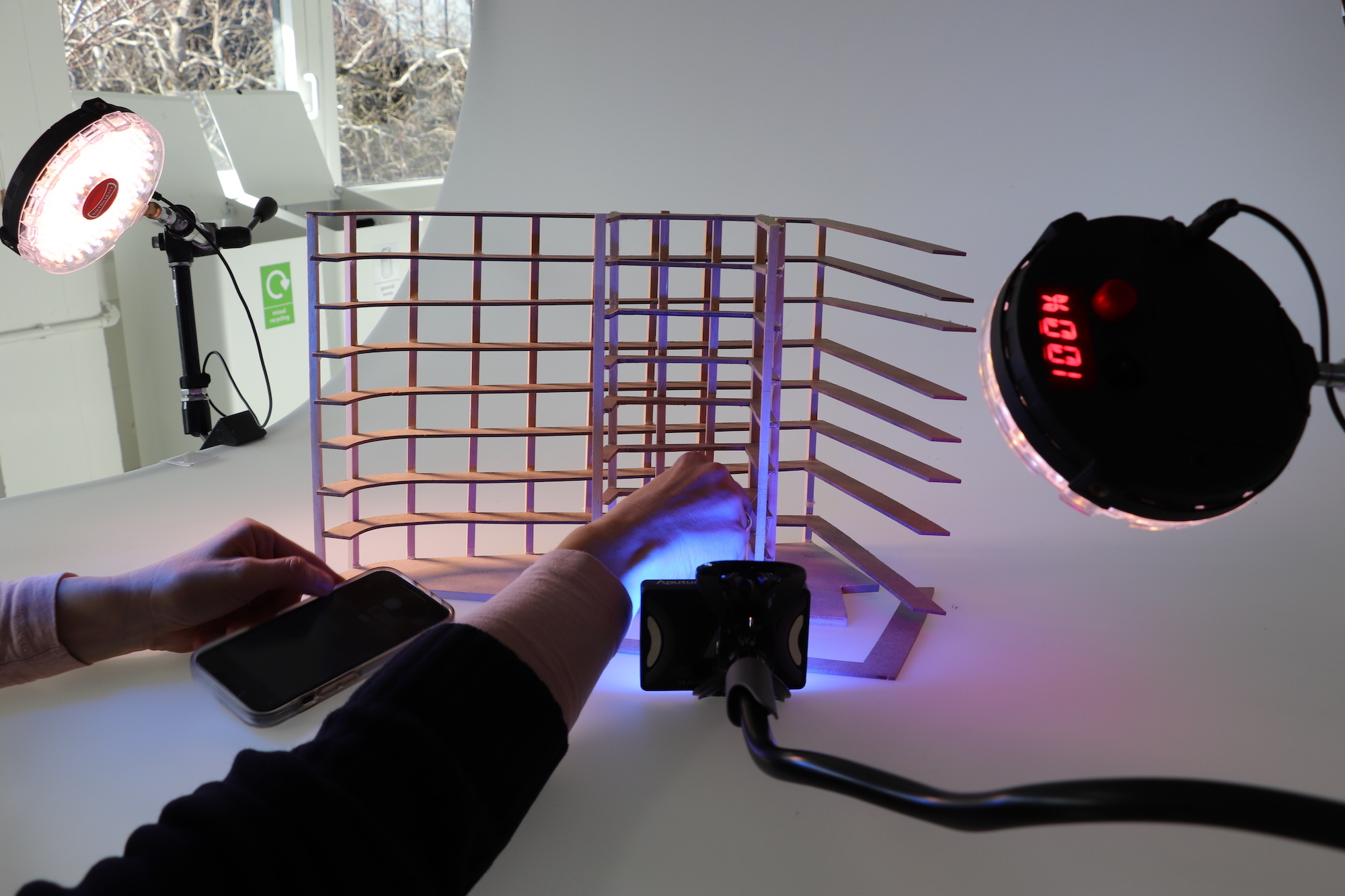 Close-up of a pair of hands adjusting a wooden model, with small lights either side and a camera resting on the surface.
