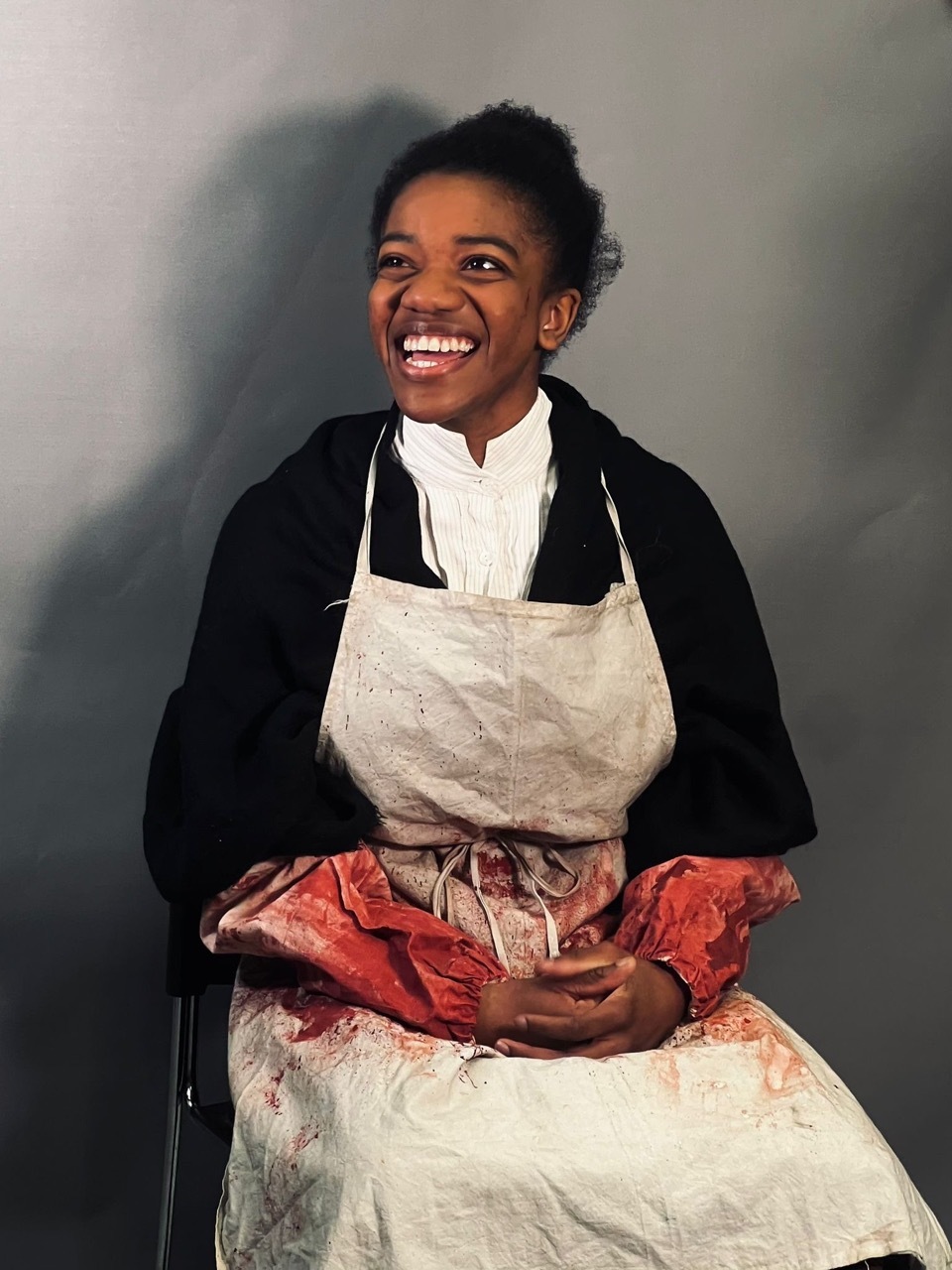 Nicole Elizabeth Phillip in costume for a performance with a white apron and bloody sleeves.