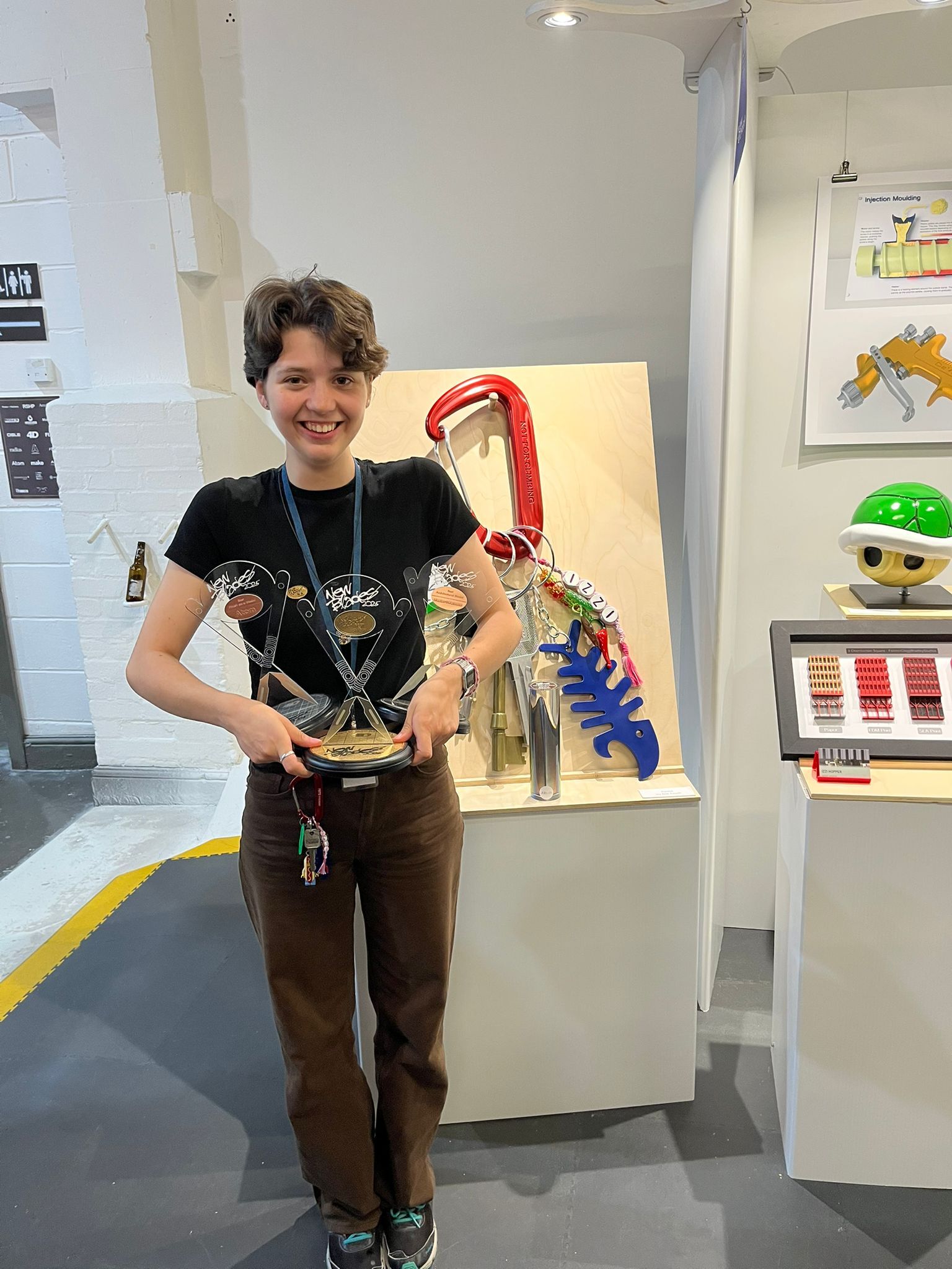 BA (Hons) Modelmaking graduate I. Hopper holding three trophies in a gallery space with white walls at New Blades Modelmaking expo, London.