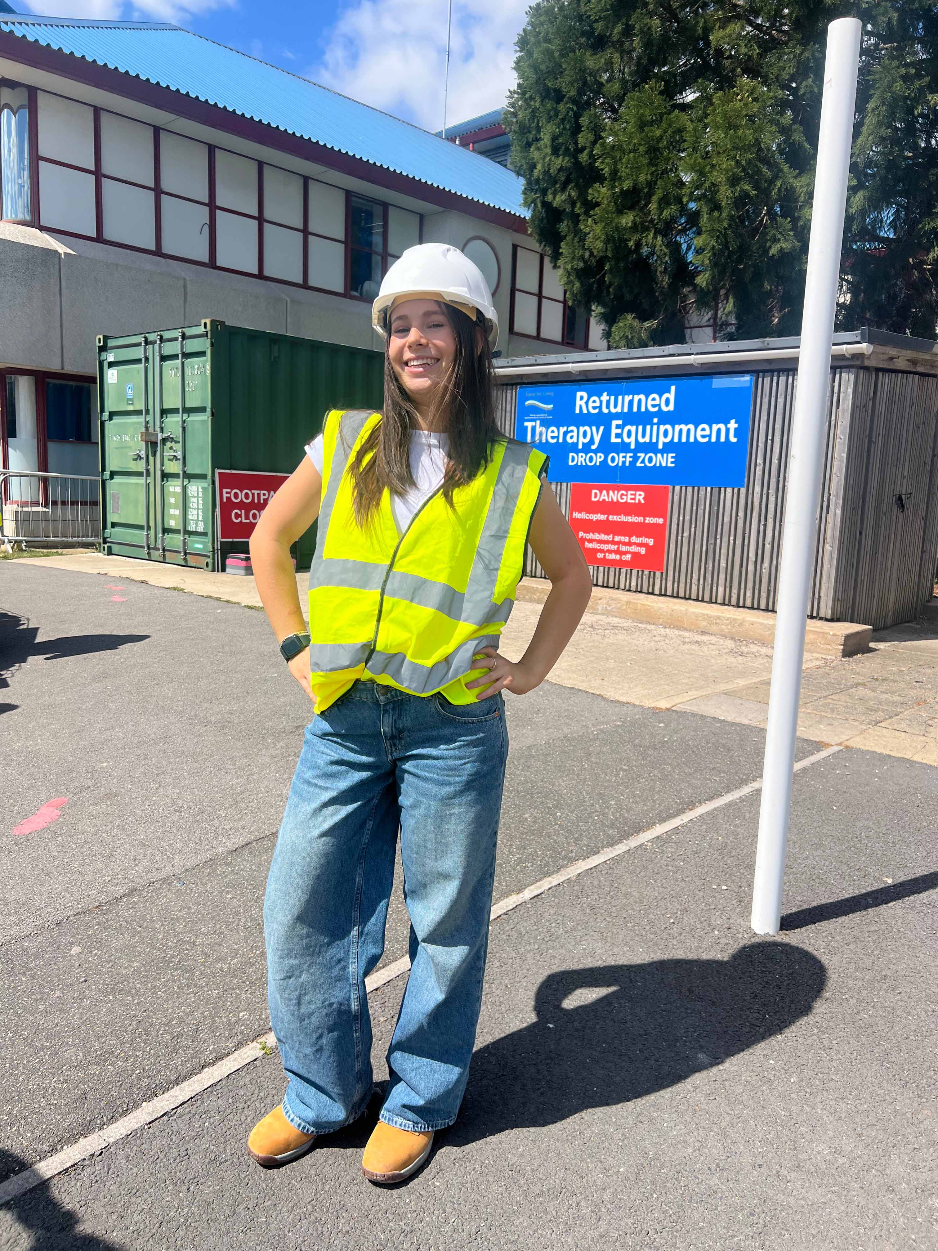 Amelia Mason stood outside Bournemouth Hospital wearing a hi-vis, white construction hat and jeans, sunny day.