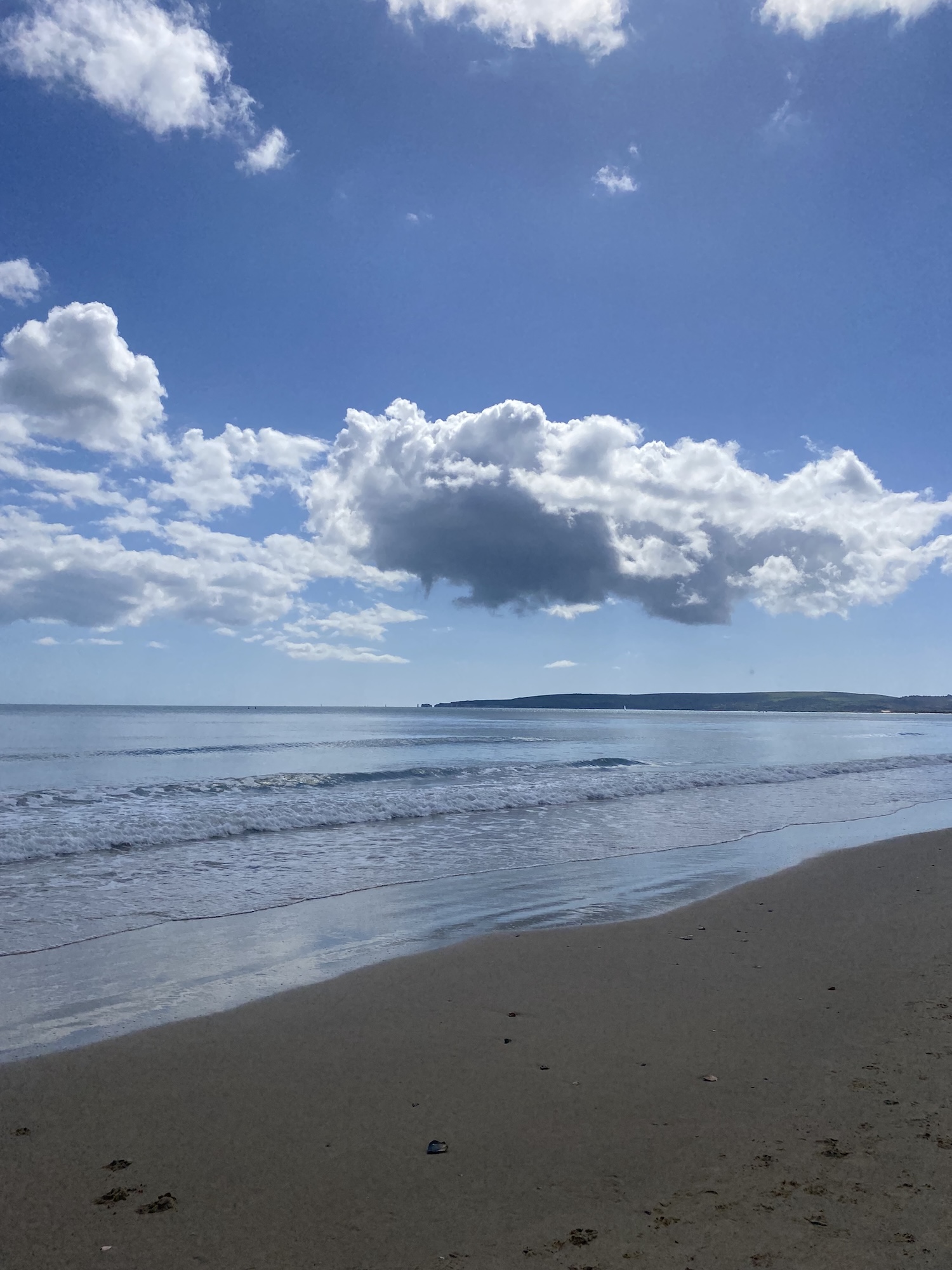 Beach and sea at Sandbanks, Poole, with cloudy sky and Isle of Purbeck in the distance.