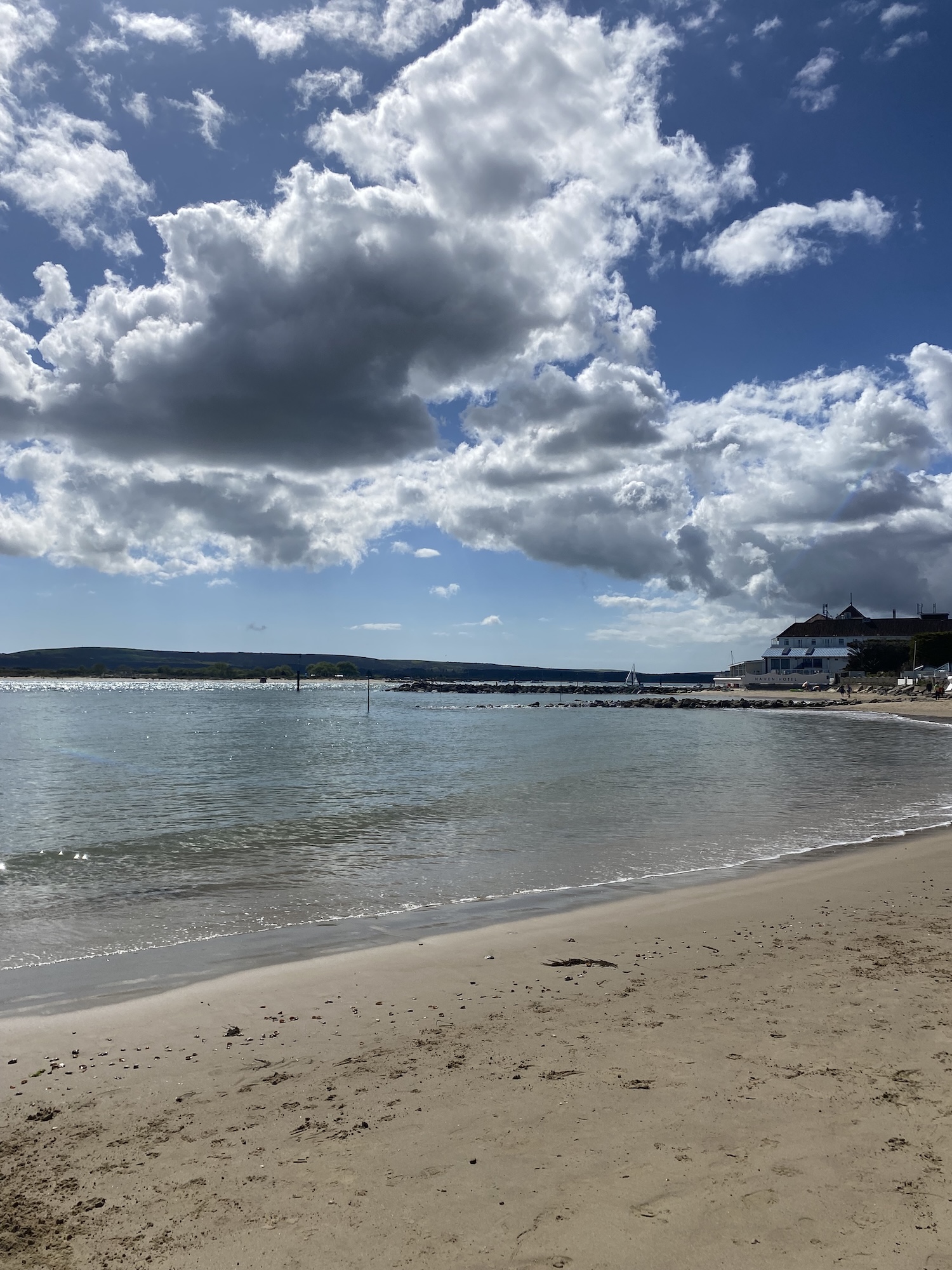 Beach and sea at Sandbanks, Poole, with cloudy sky and a hotel visible in the distance.