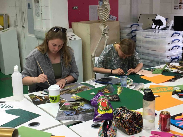 Two ladies working at tables covered in arts and crafts items.