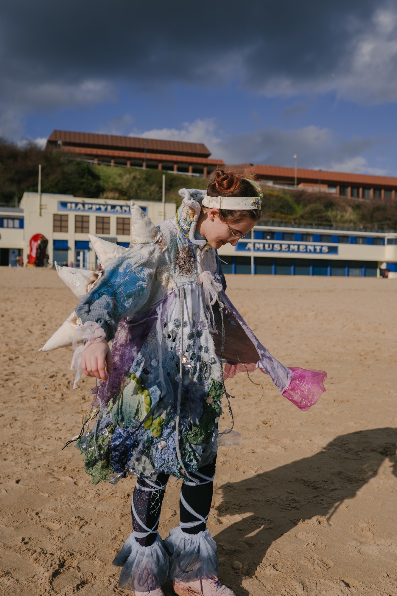 A person wearing a pollution-inspired dress on Bournemouth beach, blue, green and white with patterns and embroidery.