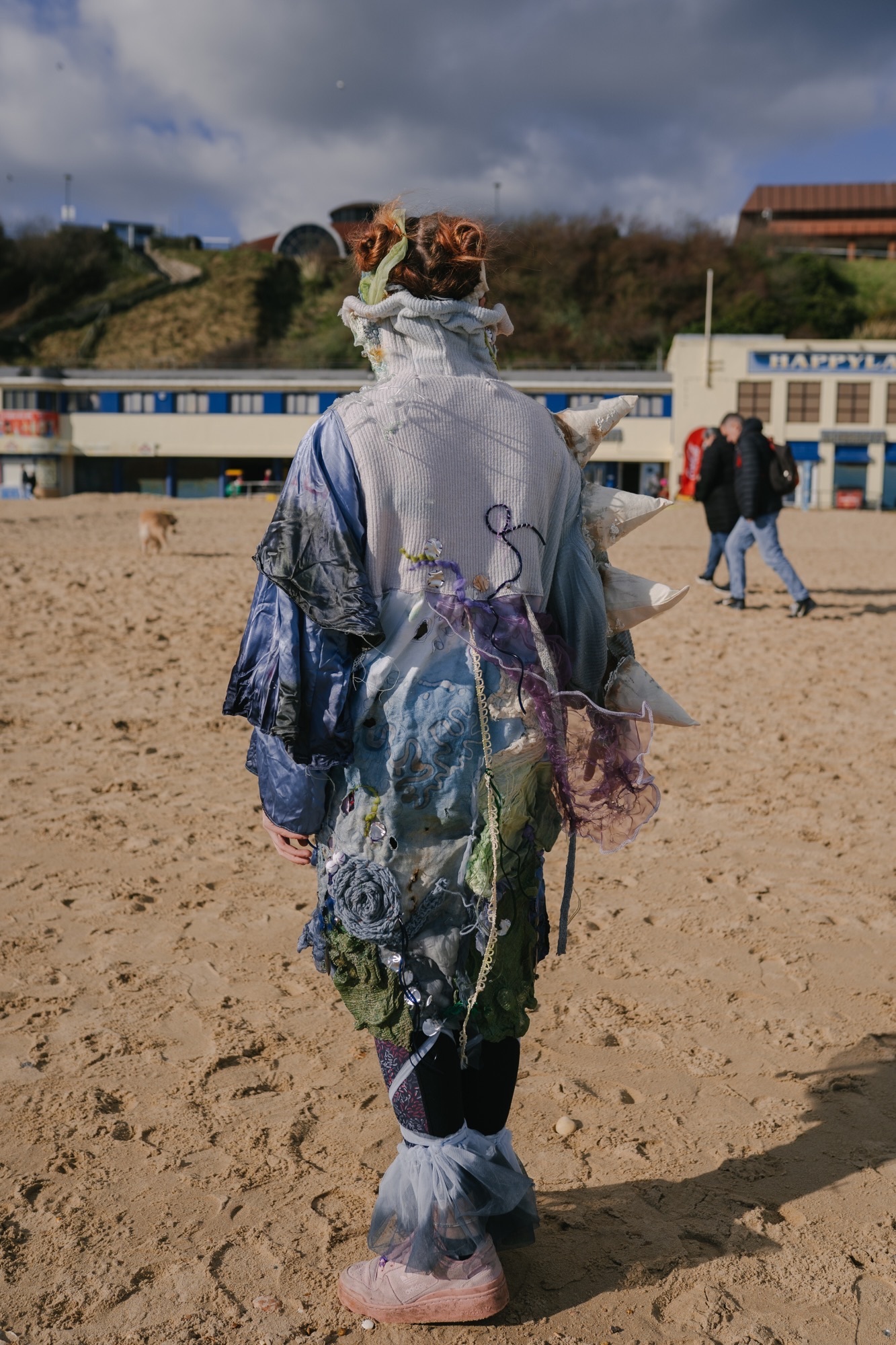 A person wearing a pollution-inspired dress on Bournemouth beach, blue, green and white with patterns and embroidery.