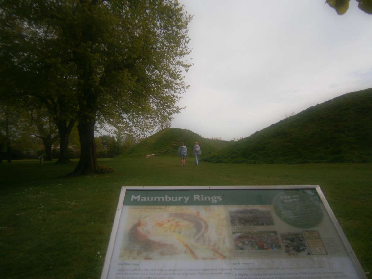 Low res image, two people walking away from an information board that reads 'Maumbury Rings'