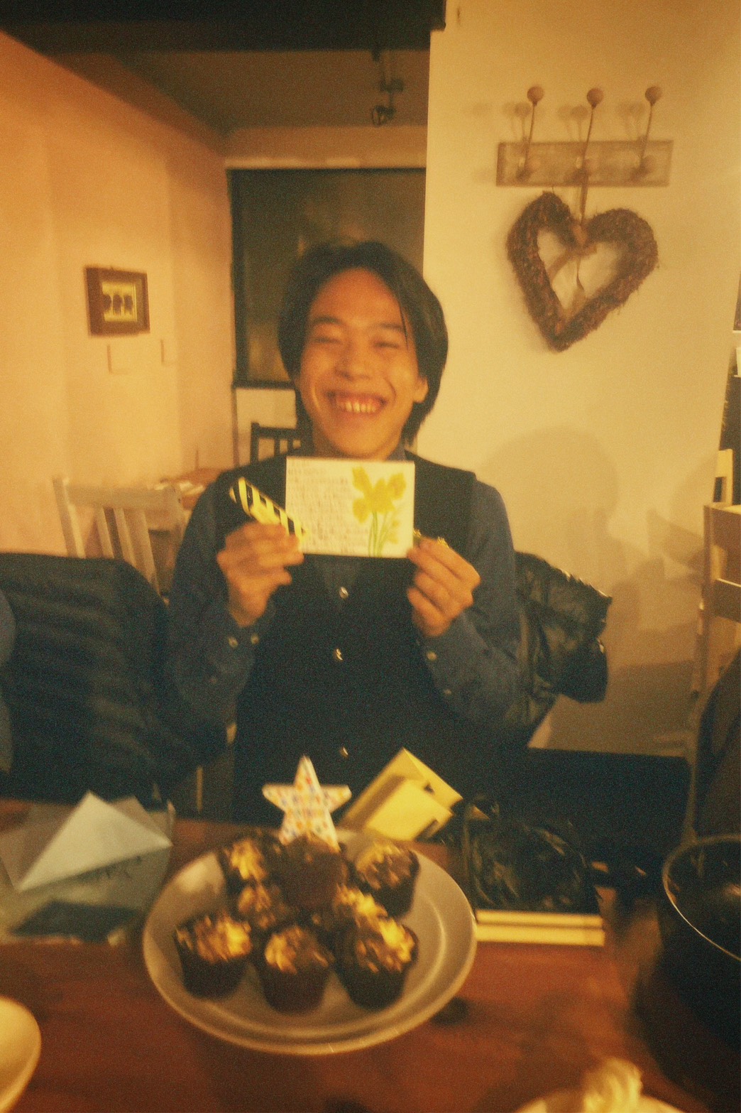 Seiji Suzuki smiling holding a flower card, birthday cupcakes below.