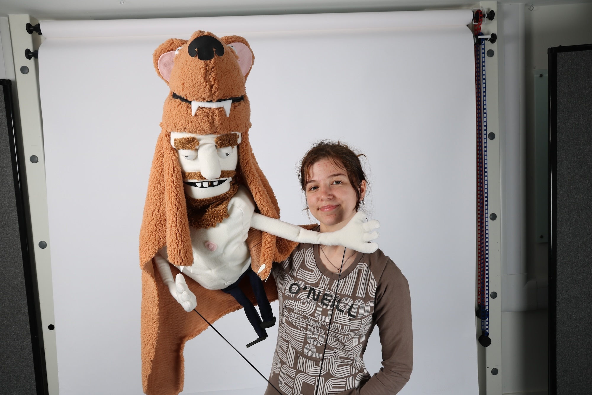 A BA (Hons) Modelmaking student holds a puppet of a shirtless bearded man wearing a brown wolf's head headdress and cloak.