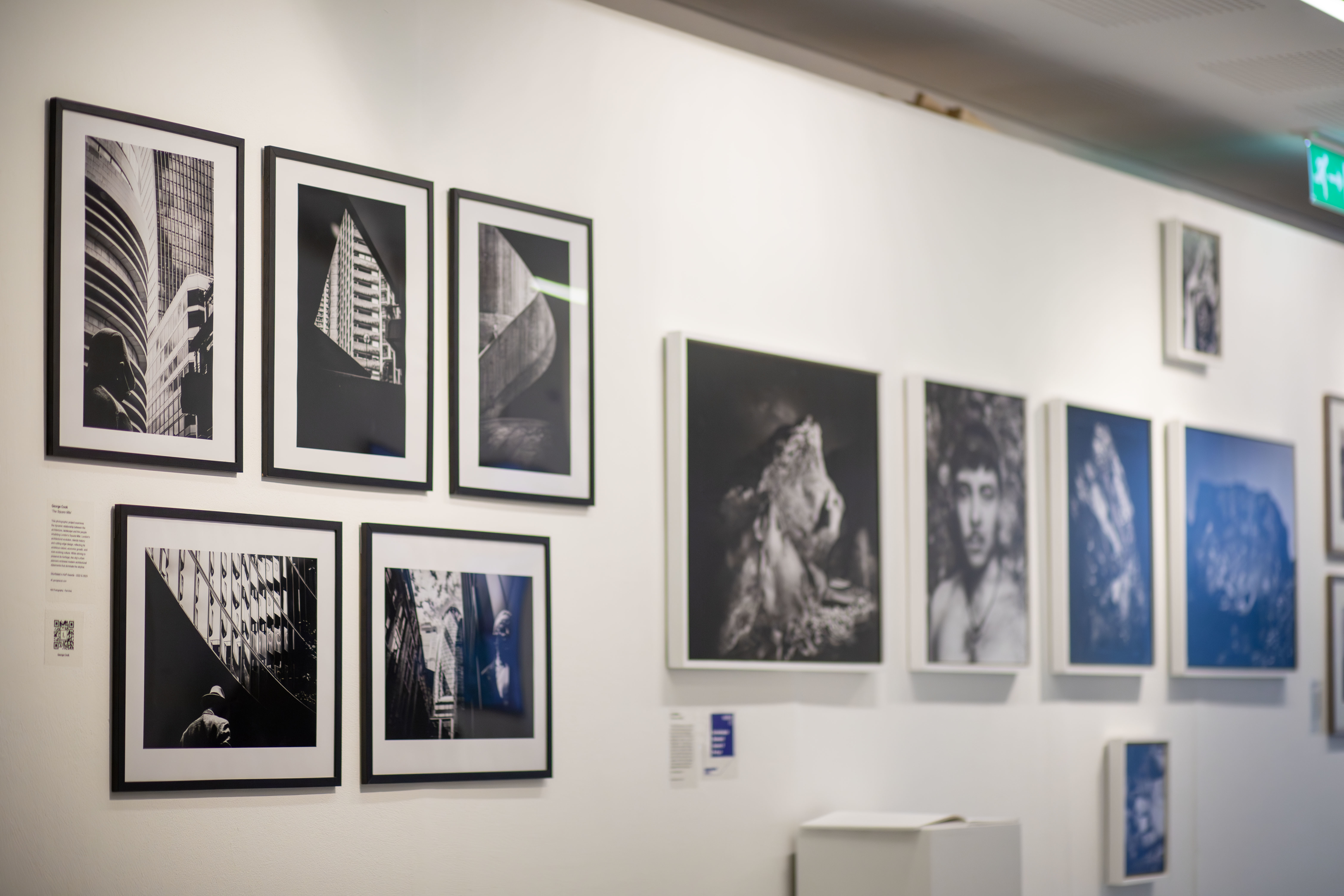A wall of TheGallery at AUB, with several framed photos and canvases on display.