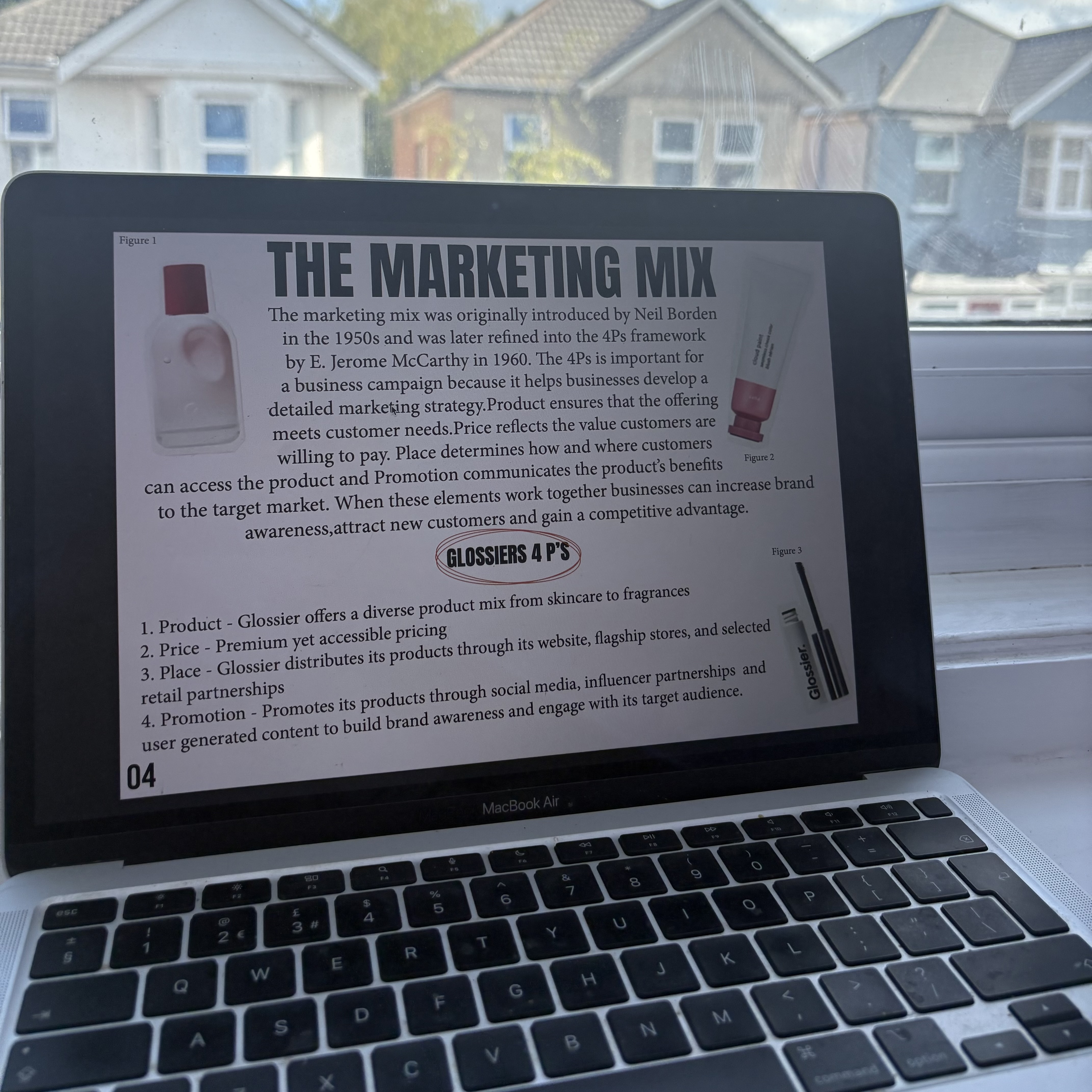 A MacBook Air displaying a presentation slide titled 'The Marketing Mix', with text about the 4Ps and a window view of houses in the background.