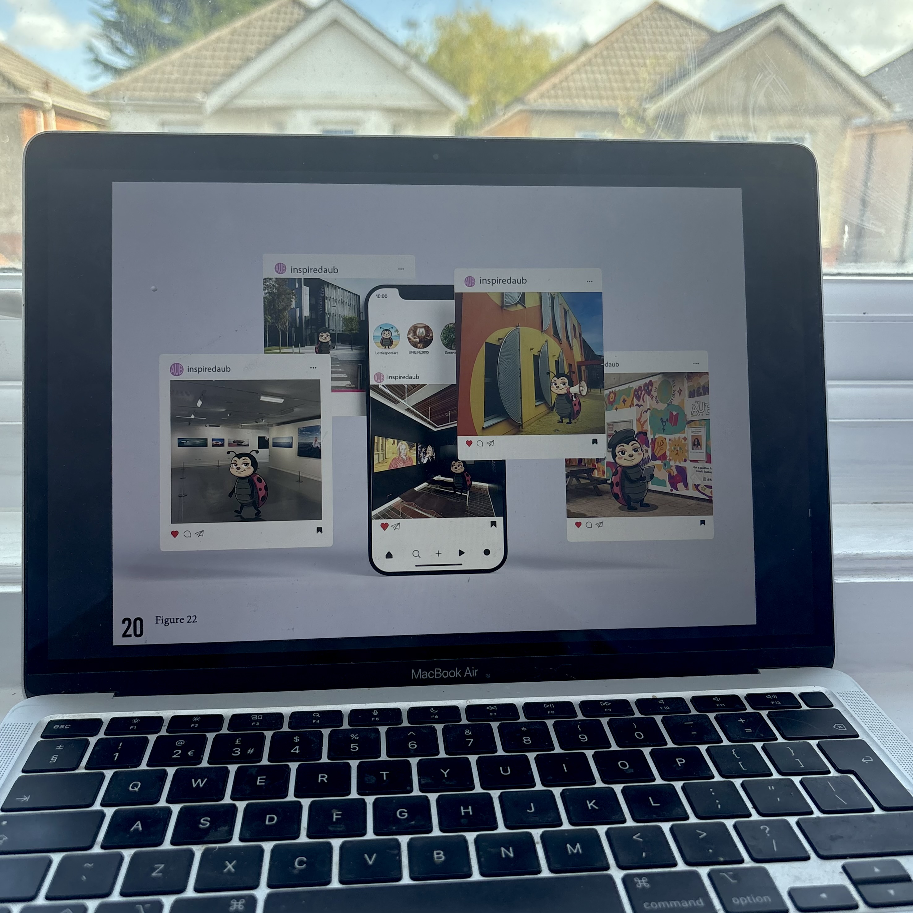 A MacBook Air shows a collage of Instagram-style posts with a cartoon mascot on screen, with a bright window and houses visible behind it.
