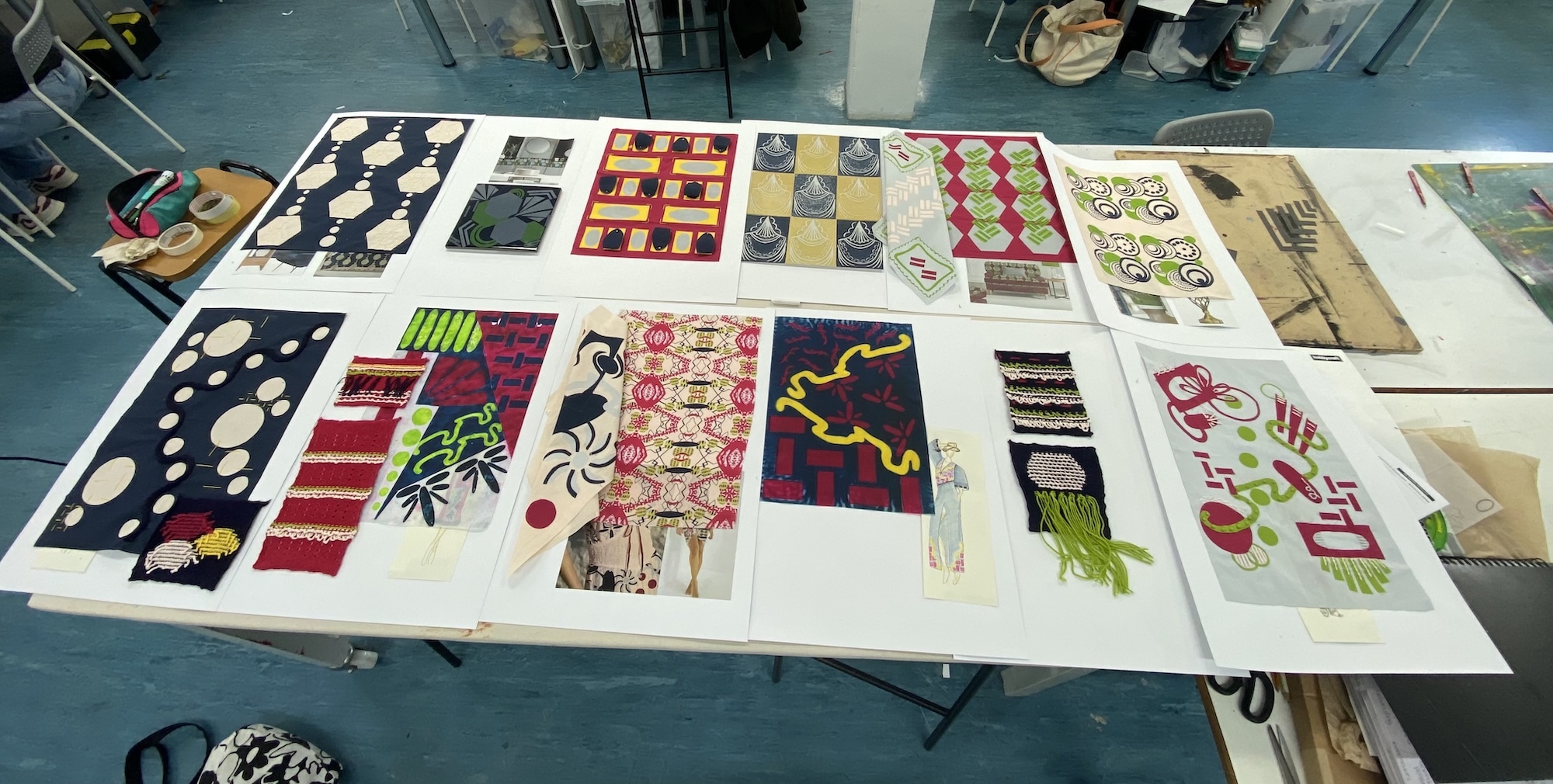 Large white table displaying multiple colourful textile samples and fabric swatches arranged in rows on grey floor.