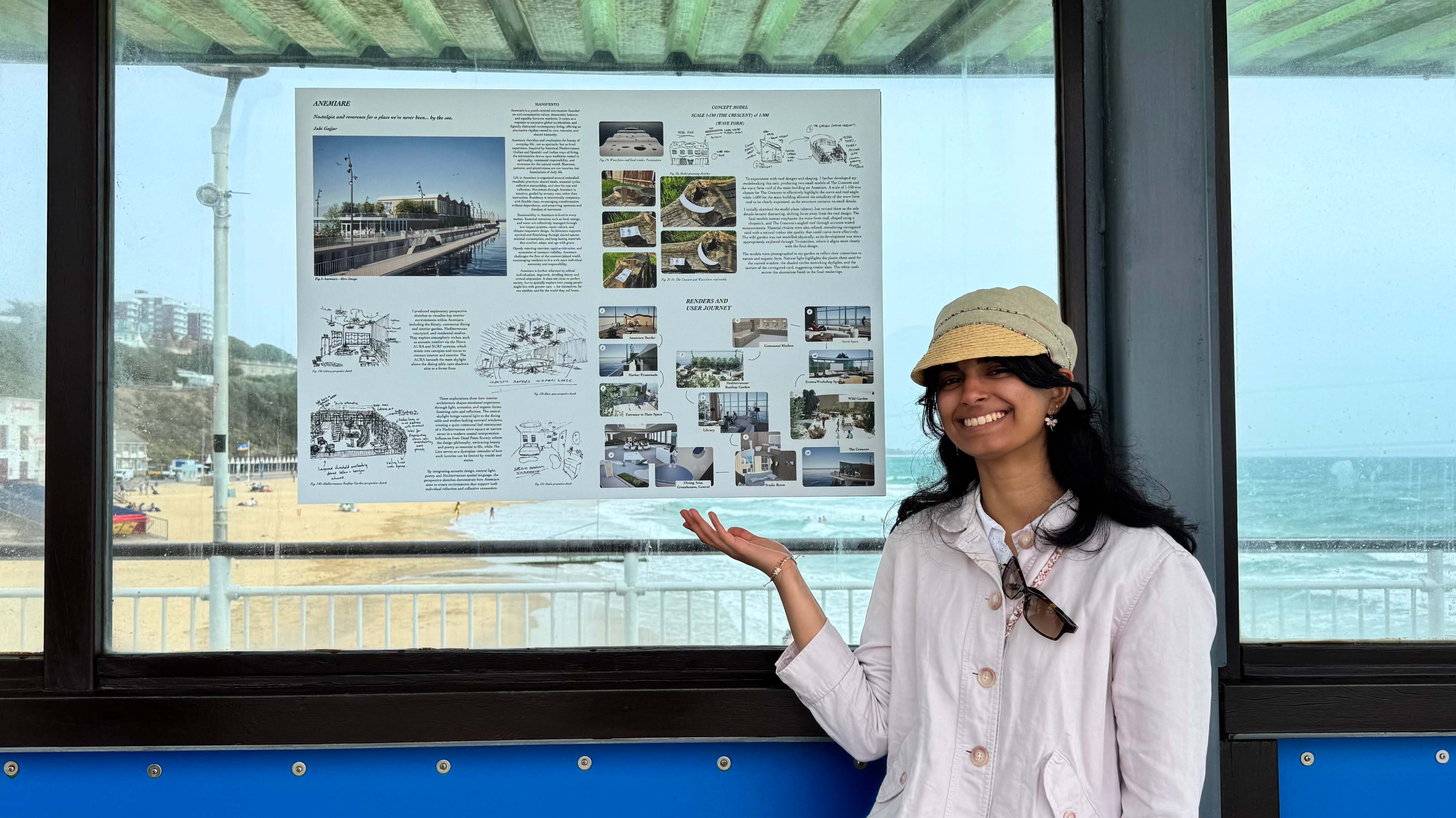 Juhi stood by a poster of her work on Bournemouth Pier, showing sketch illustrations and photo renders alongside words. She is wearing a hat and white shirt, stood smiling.