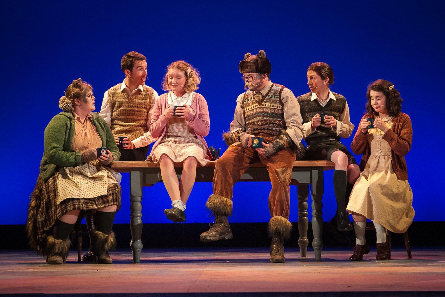 Actors on stage sitting on a table