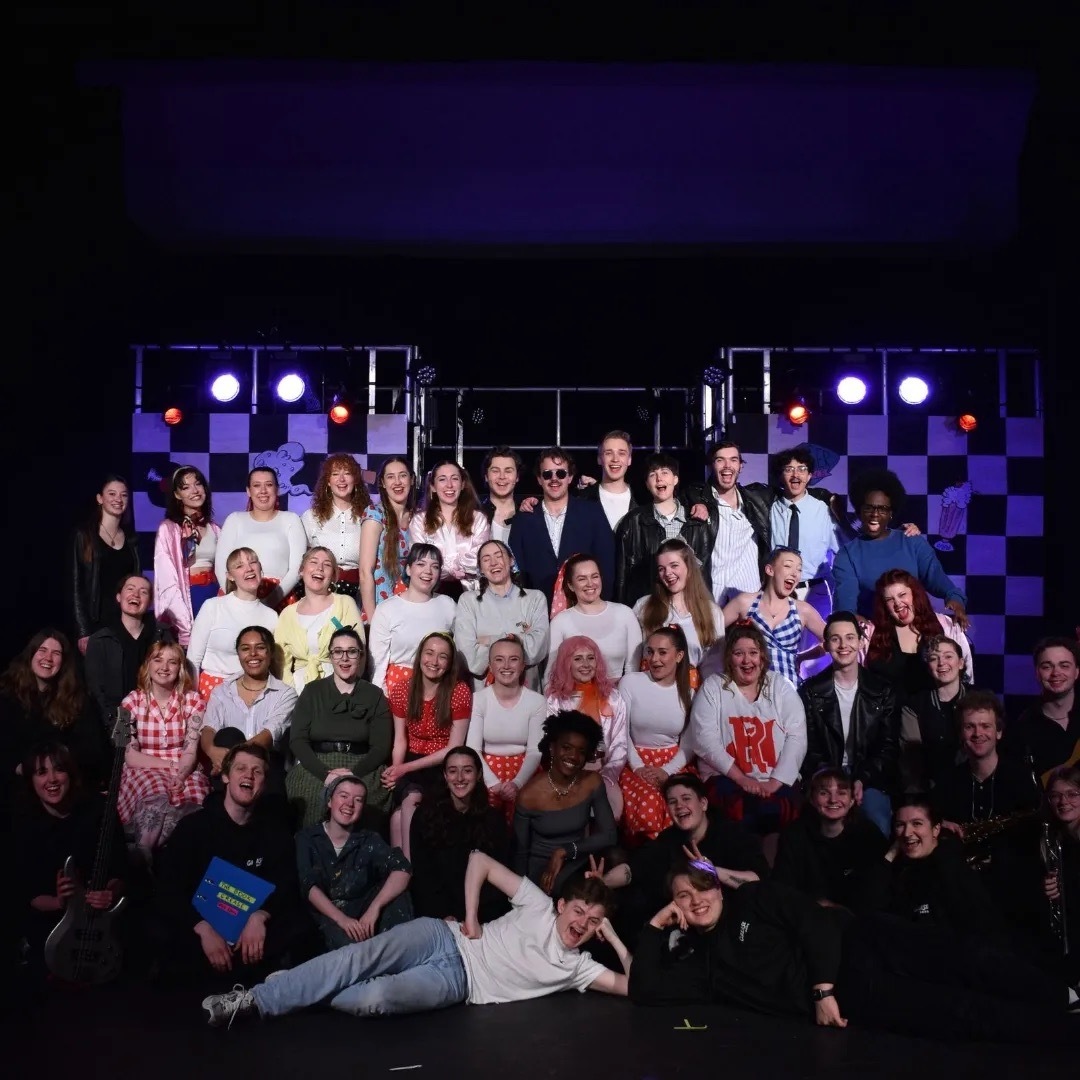Nicole Elizabeth Phillip with the Grease cast of PARTS society on-stage, purple lights.