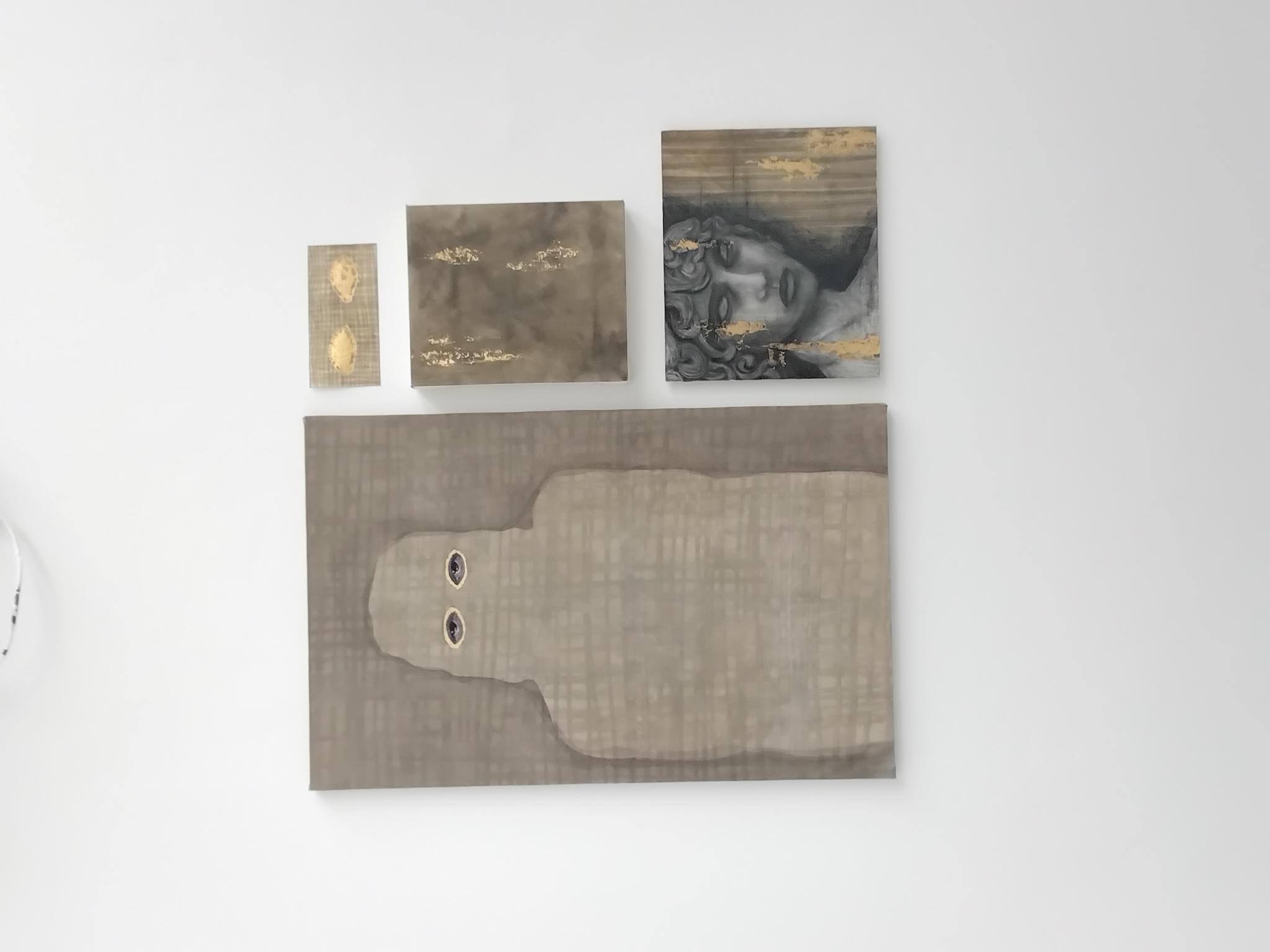 Two abstract art pieces and a portrait are displayed on a white wall. The larger piece features a grey silhouette with two eyes, while the smaller works include a patterned rectangular piece and a portrait with intricate designs.